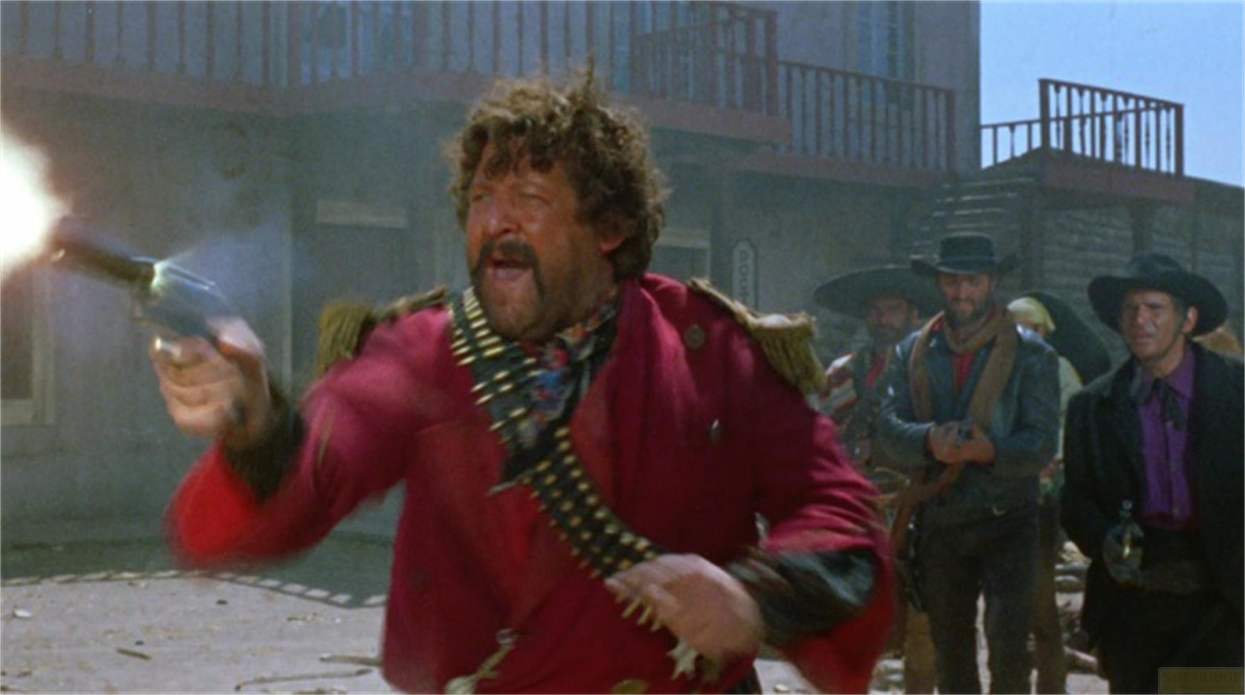 Uomo in giacca rossa spara con rivoltella, altri uomini in abiti Western dietro.