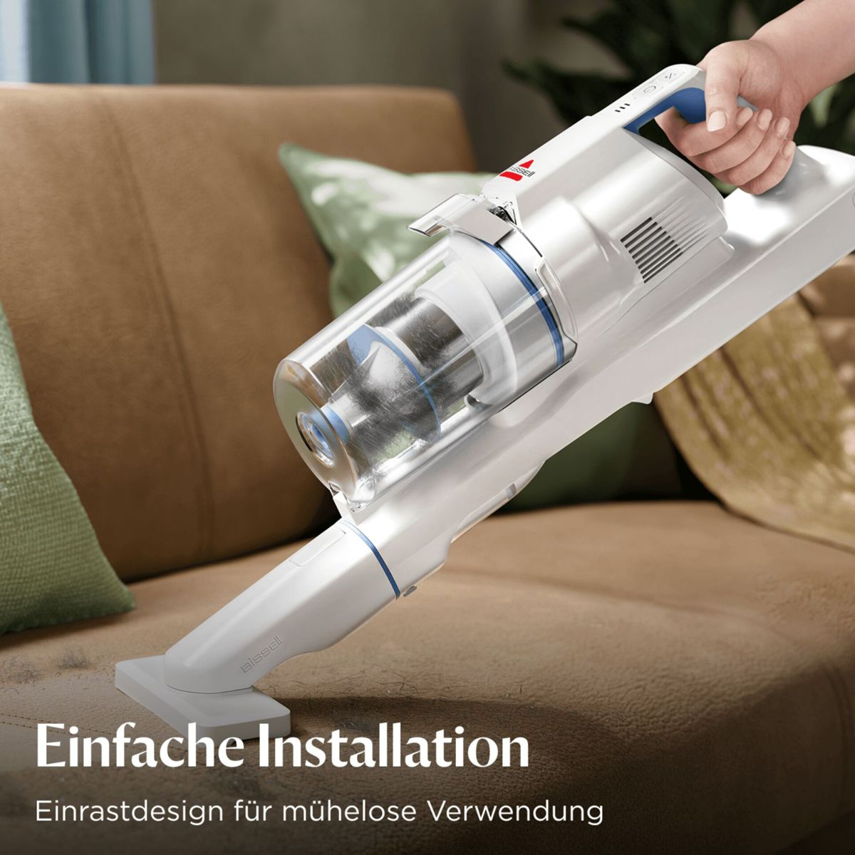 Eine Hand hält einen weißen Akku-Staubsauger, der auf einem braunen Sofa verwendet wird.