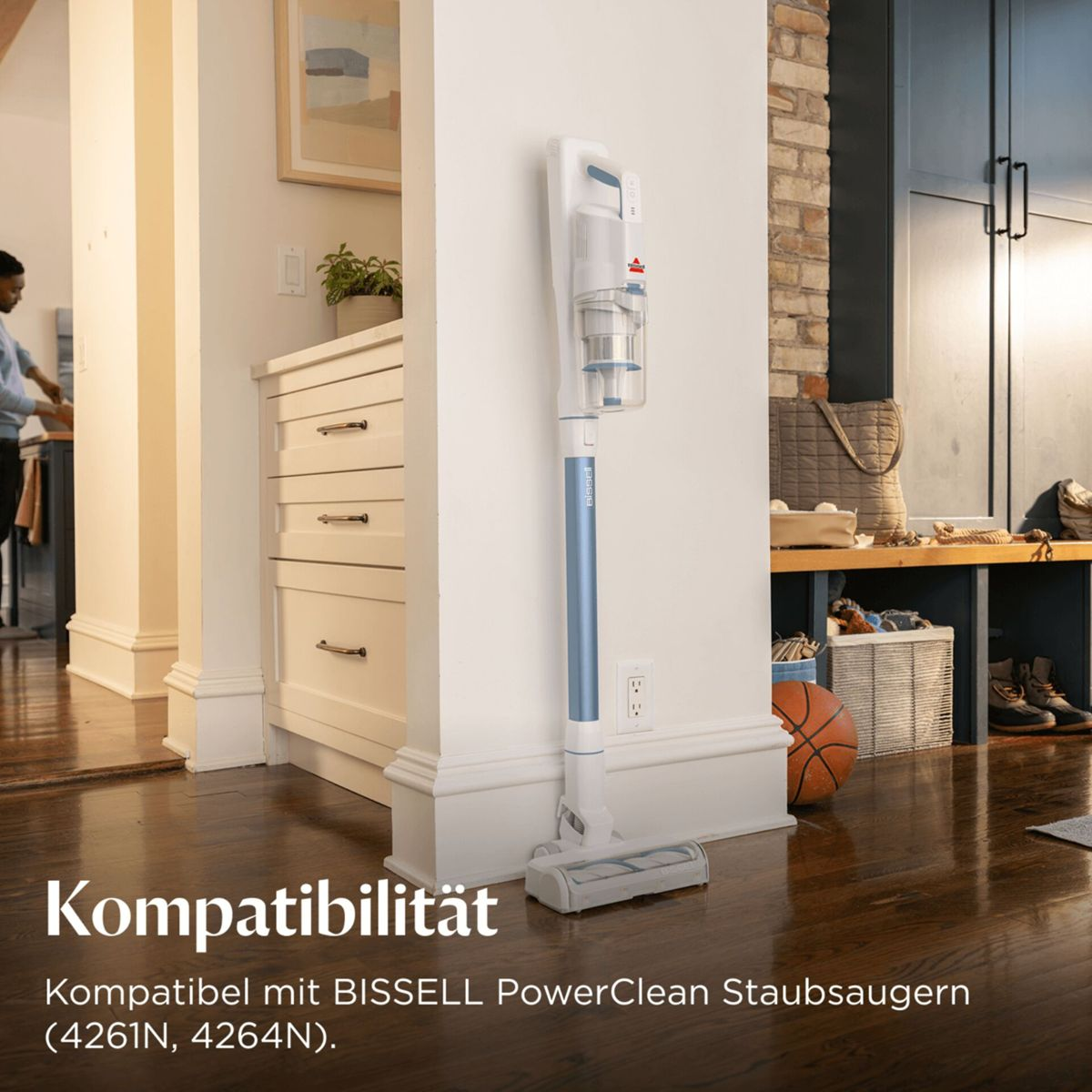 Ein blauer und weißer Akku-Staubsauger steht an einer weißen Wand neben einer Kommode.