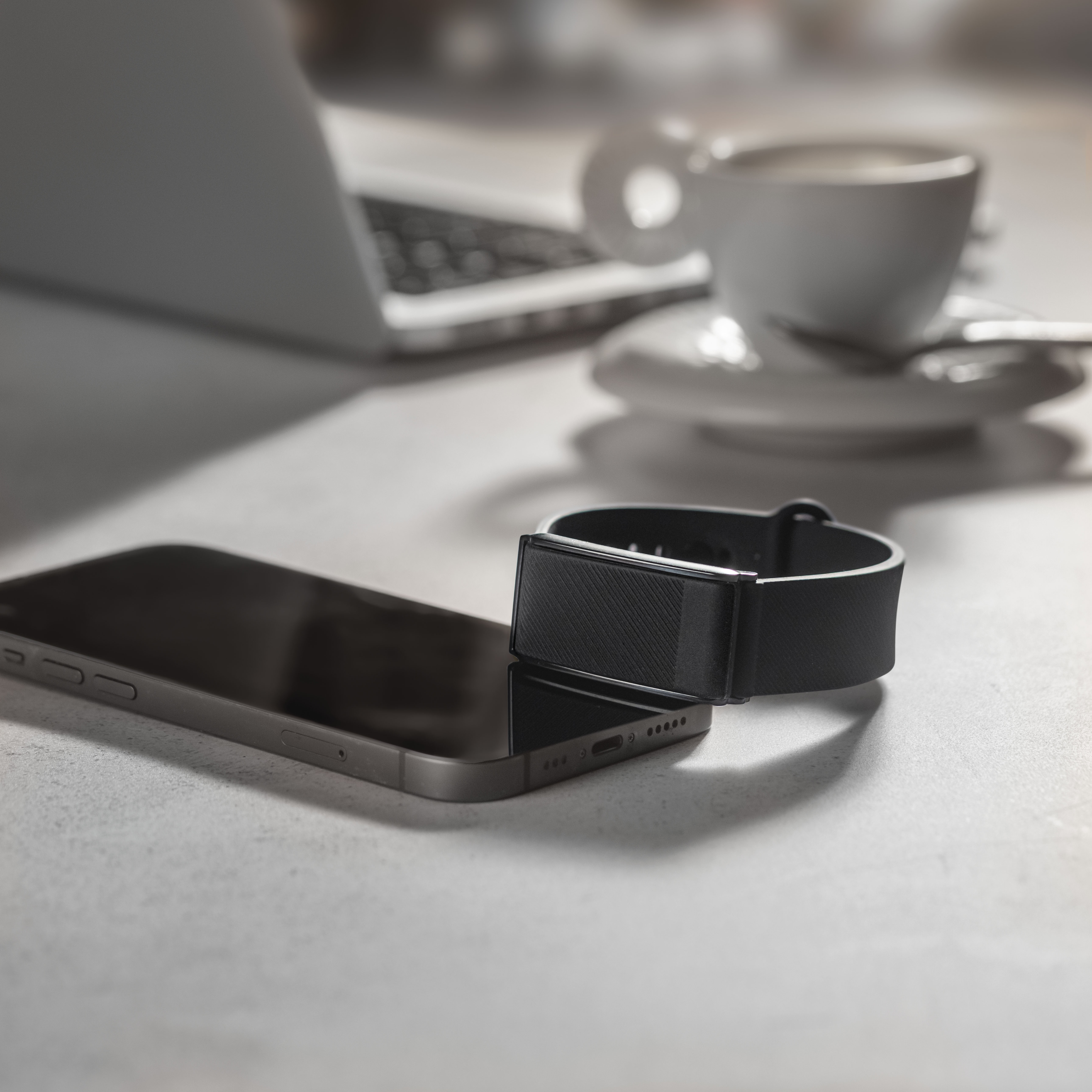 Un smartphone negro junto a un rastreador de actividad física. Al fondo, una taza de café.