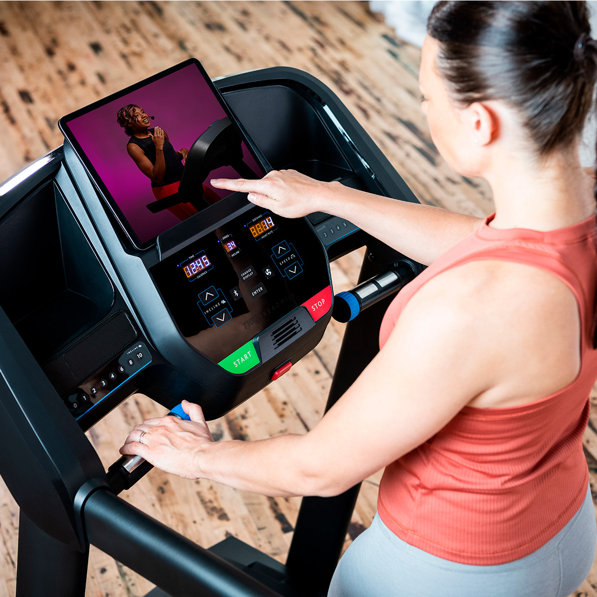 Mujer usa cinta con tableta mostrando clase de fitness.