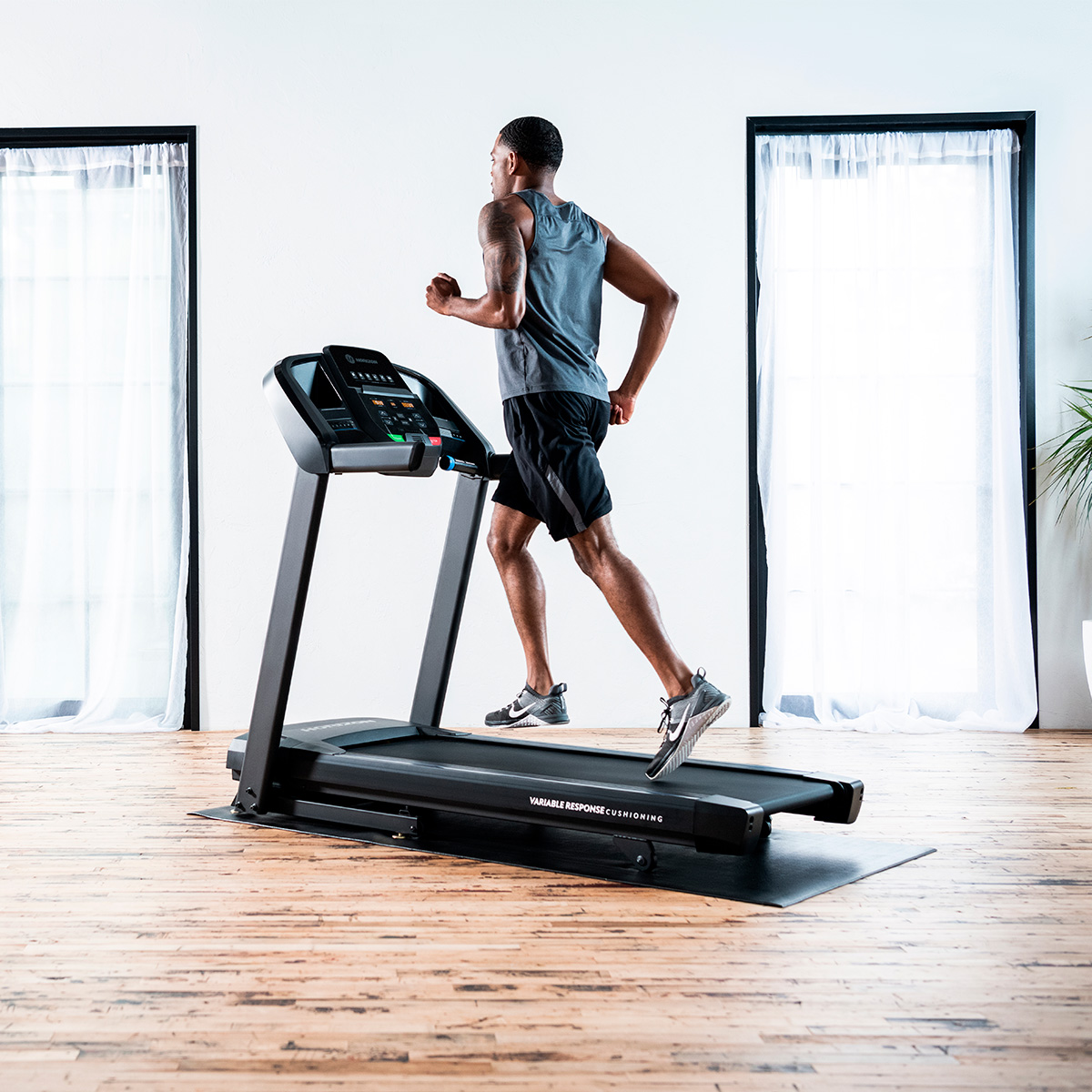 Un hombre corre en una cinta de correr en una habitación luminosa con suelo de madera.