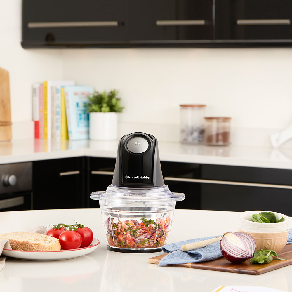 Ein Russell Hobbs Zerkleinerer mit gehacktem Gemüse, Brot und Tomaten auf einer Küchentheke.