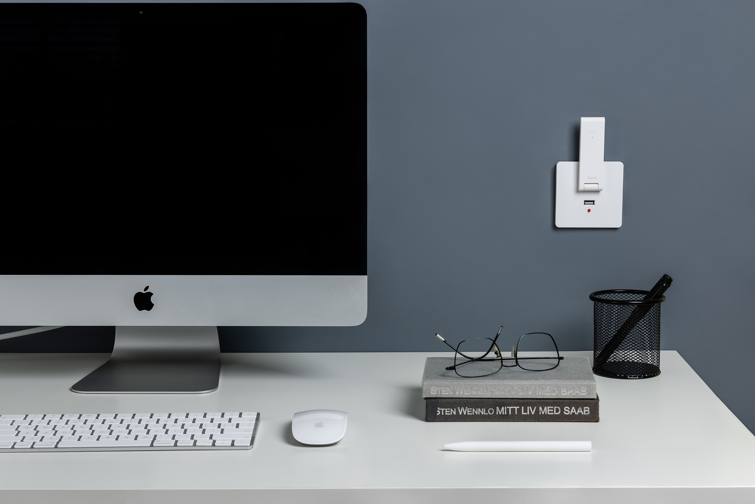 Un iMac de Apple, teclado, ratón, gafas, bolígrafo y portalápices en un escritorio.
