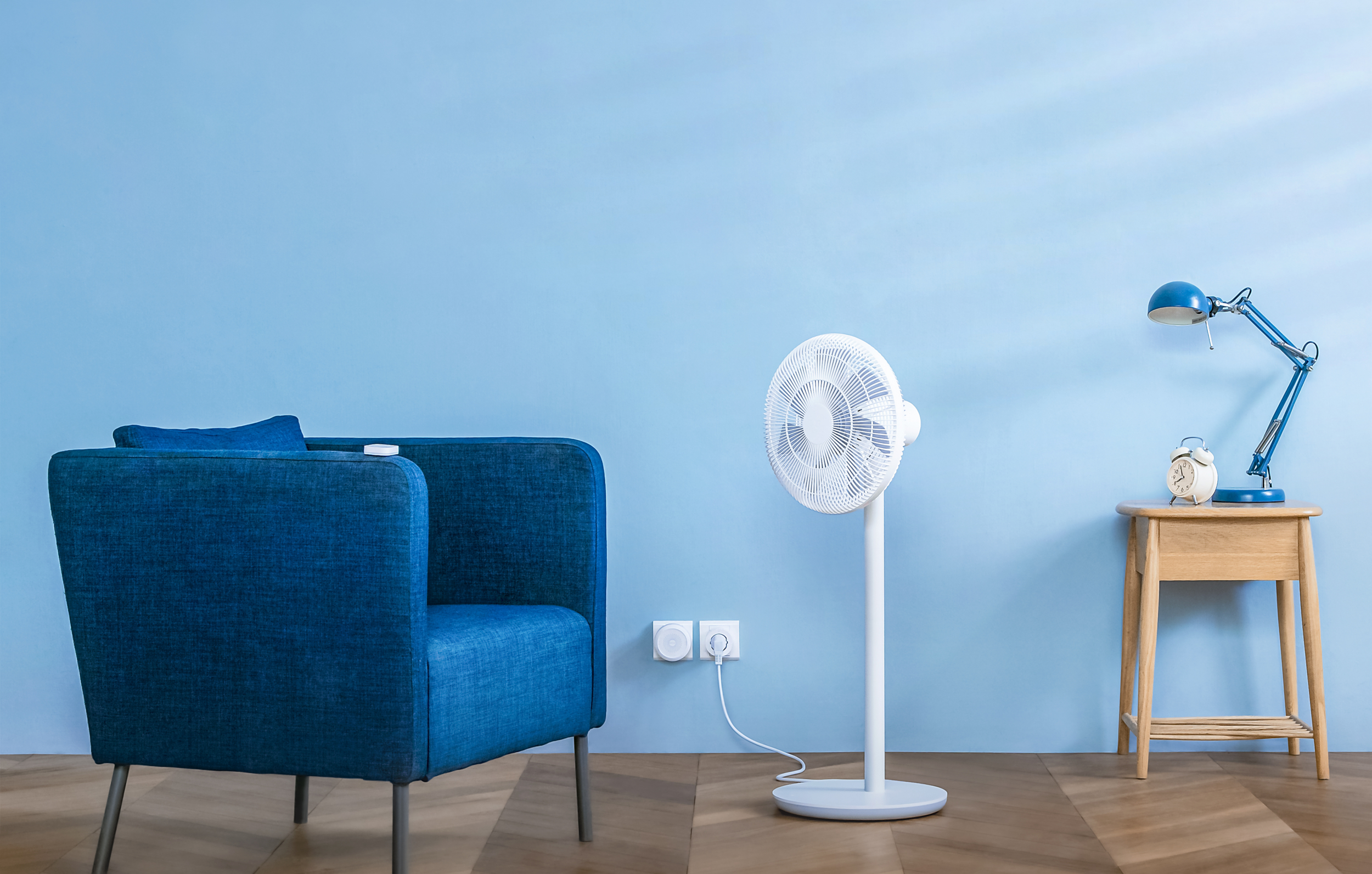 Ein blauer Sessel, ein weißer Ventilator und ein Nachttisch mit Lampe.