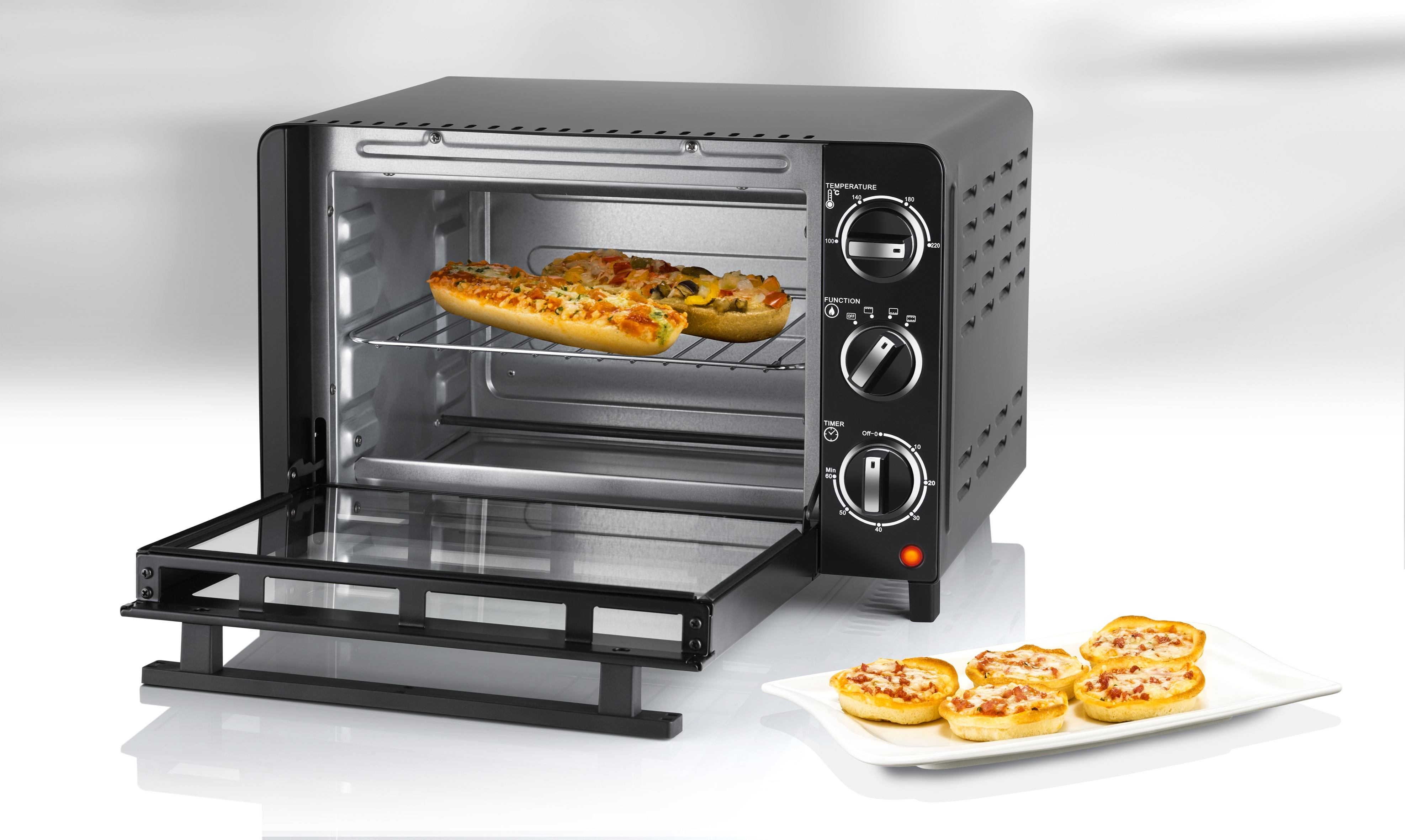 Ein schwarzer Tischofen mit geöffneter Tür, zwei belegte Baguettes auf dem Rost und Mini-Pizzen.