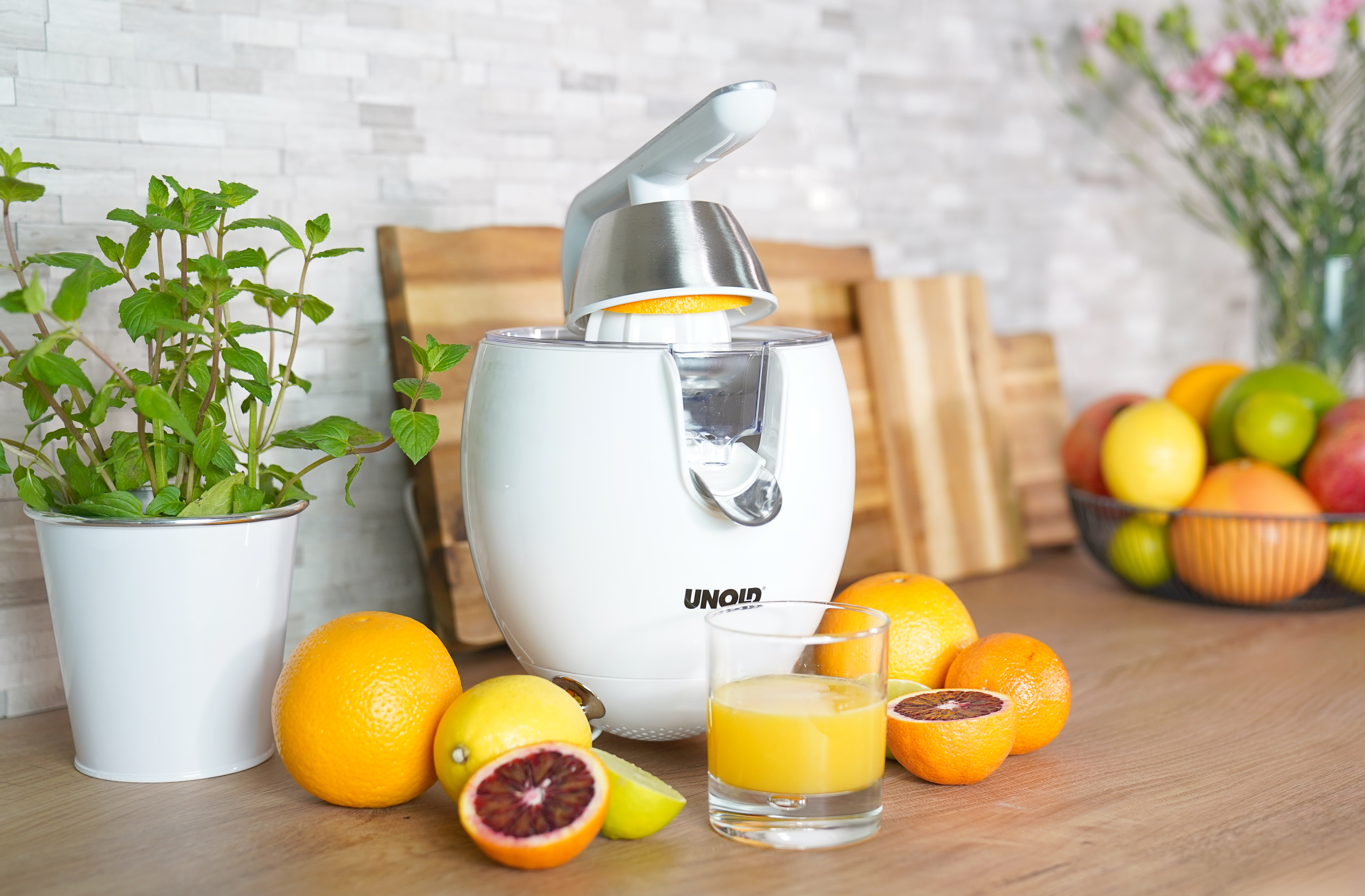 Ein weißer Entsafter mit Orangen, Zitronen und Minze auf einem Holztisch.