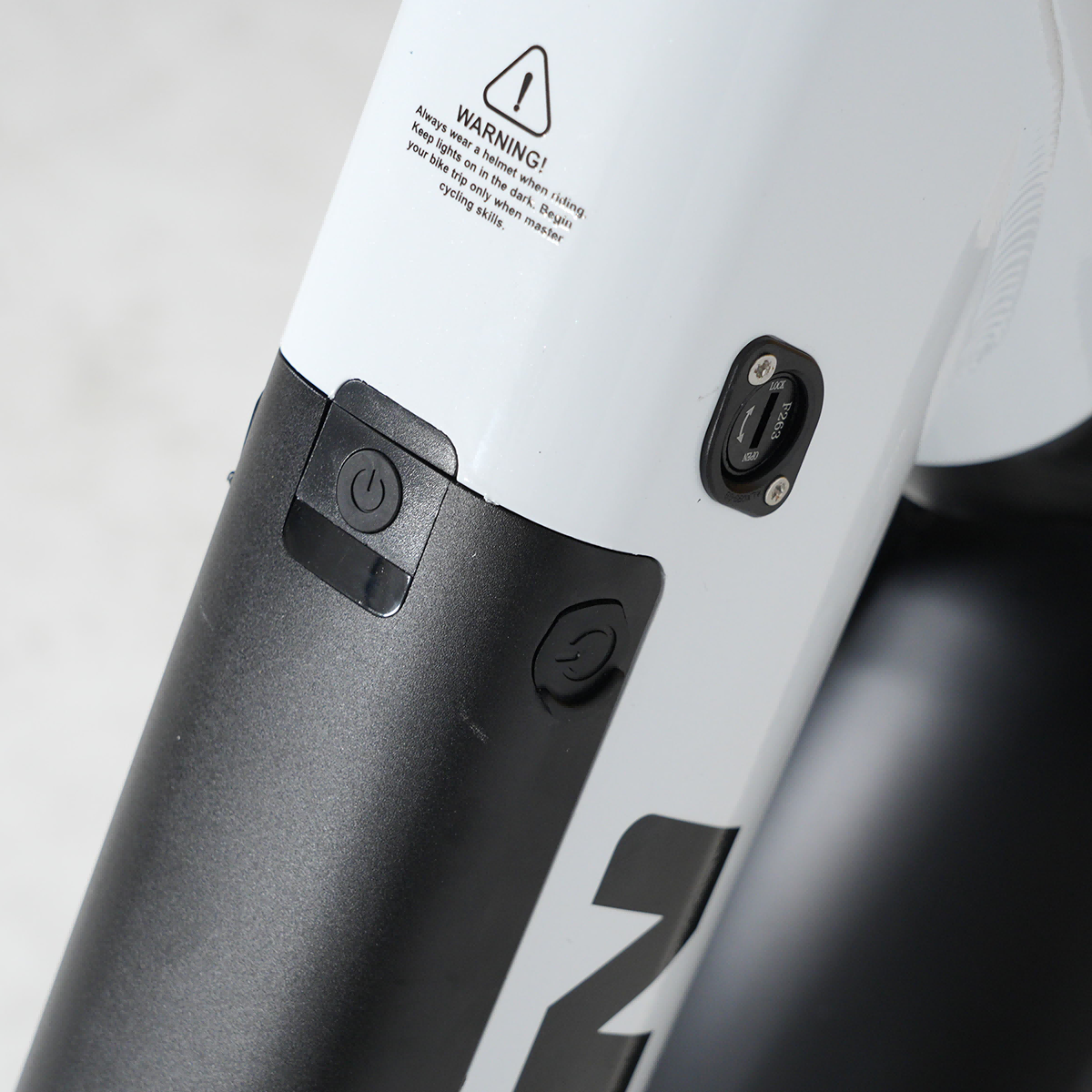 Zbliżenie białej ramy roweru z czarnymi elementami sterującymi i etykietami ostrzegawczymi.