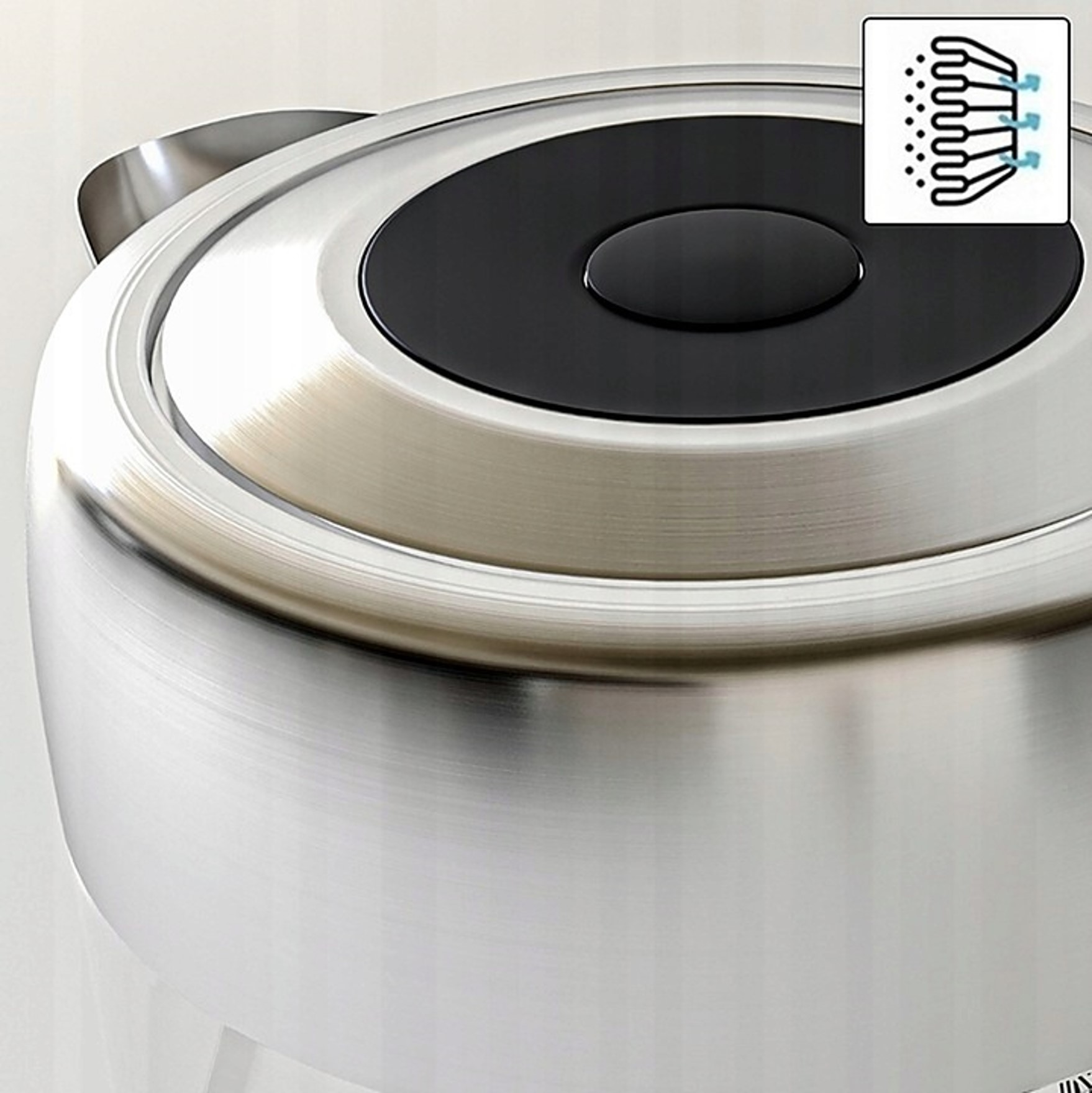 Zbliżenie srebrnego czajnika z czarną pokrywą i symbolem.