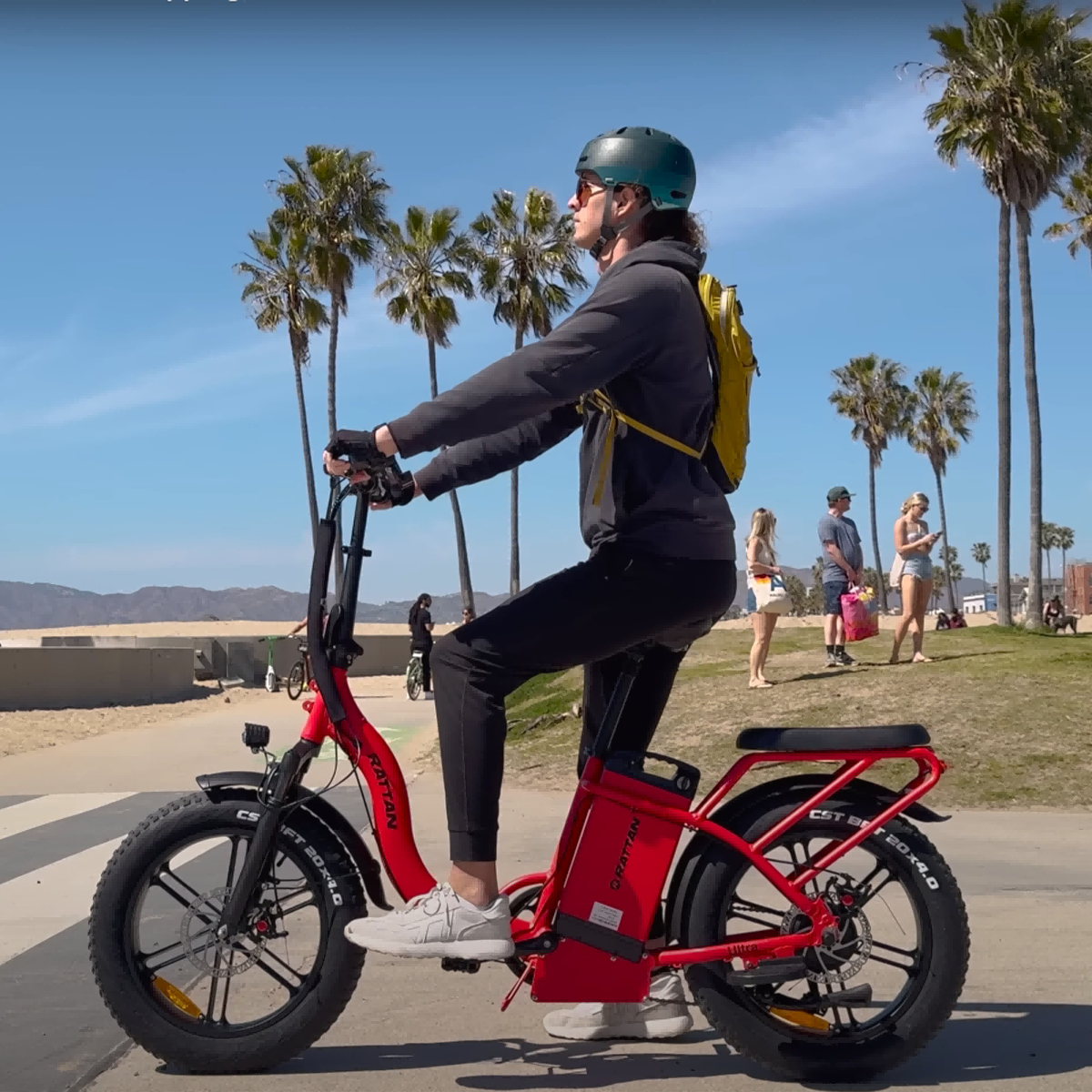 Mężczyzna na czerwonym rowerze elektrycznym z plecakiem jedzie plażą.