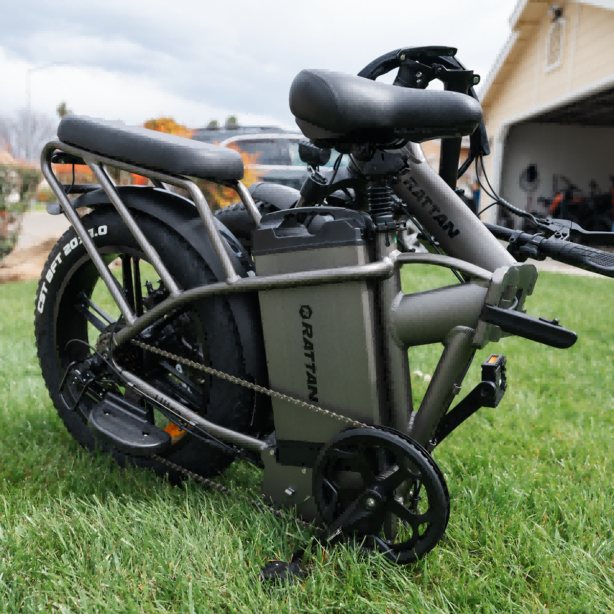 Szary rower elektryczny z szerokimi oponami na zielonej trawie. Posiada baterię i łańcuch.