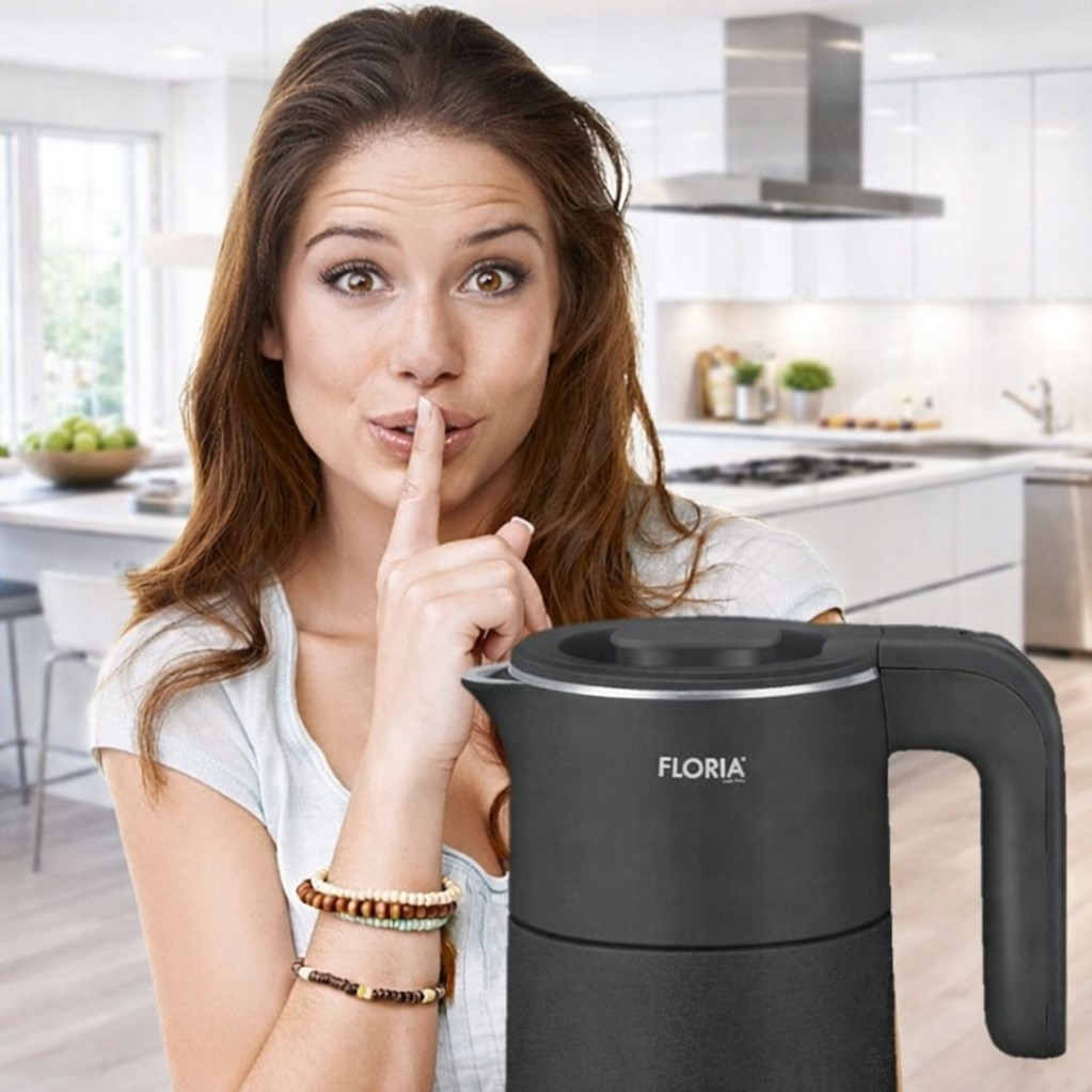 Kobieta z palcem na ustach obok czajnika w kuchni.