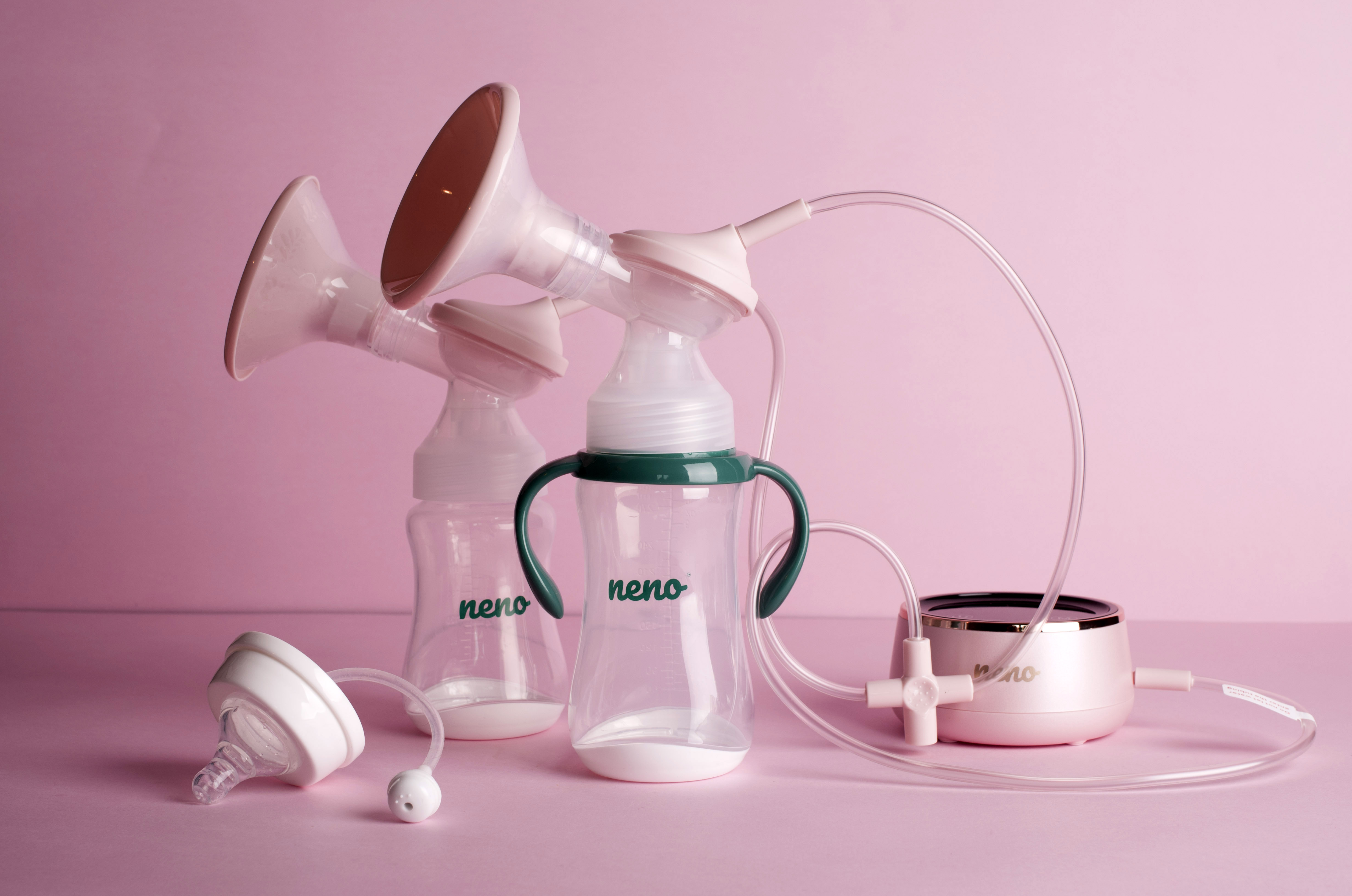 Dwie butelki laktatora z rurkami i różowe urządzenie na różowym tle.