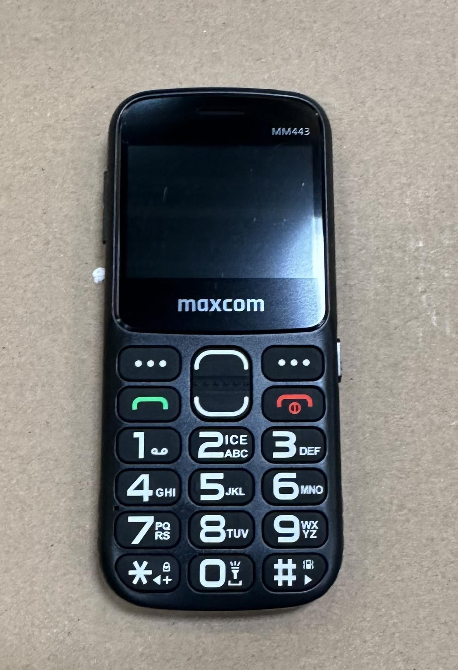 Czarny telefon komórkowy Maxcom MM443 z przyciskami leży na szarej powierzchni.