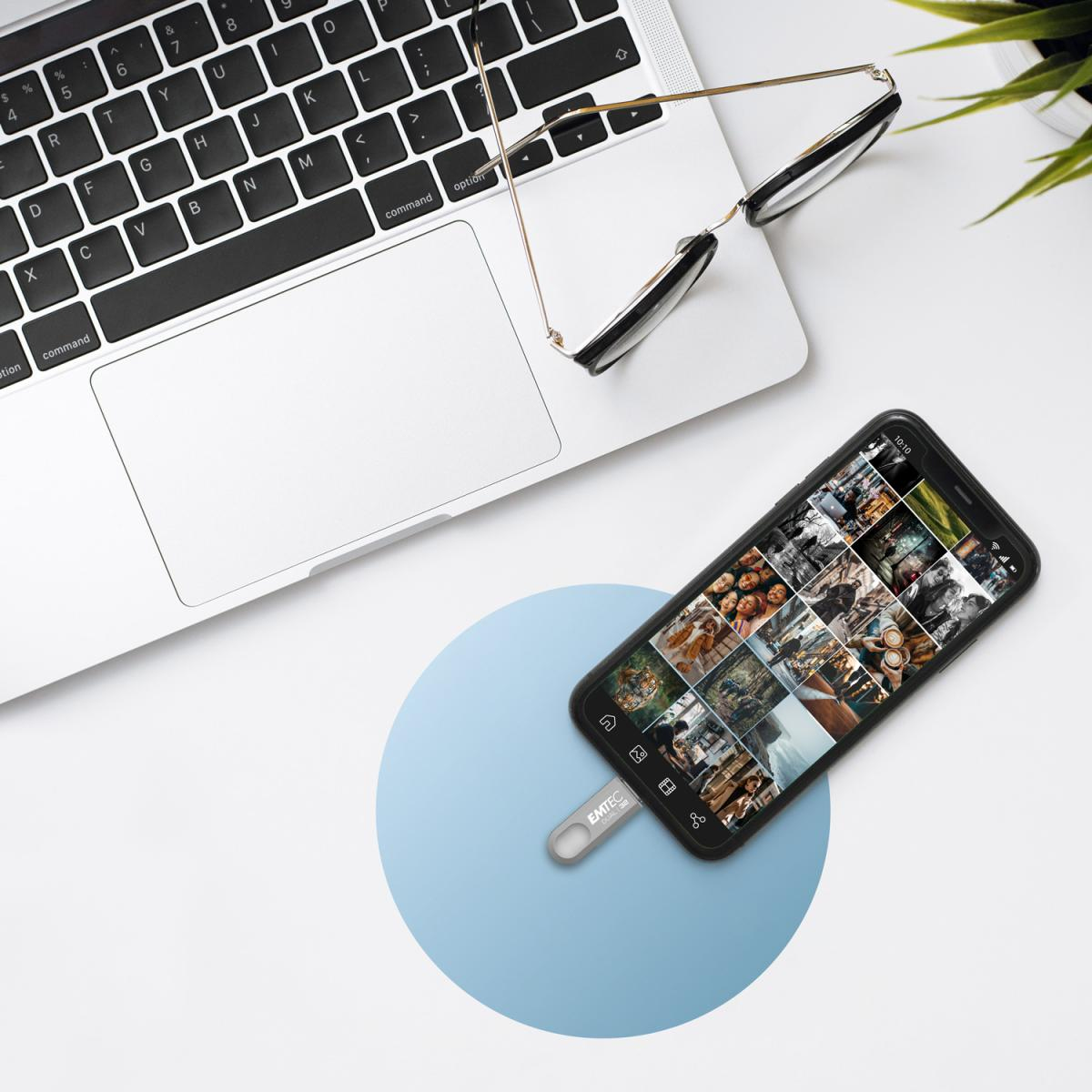 Un laptop, uno smartphone con foto, una chiavetta USB e occhiali su un tavolo.