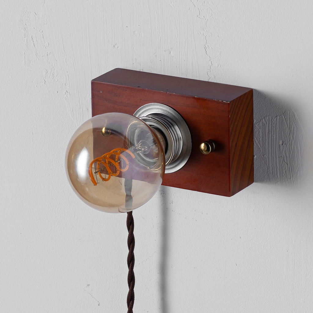 Bombilla Edison vintage con filamento expuesto en montura de madera sobre pared texturizada.