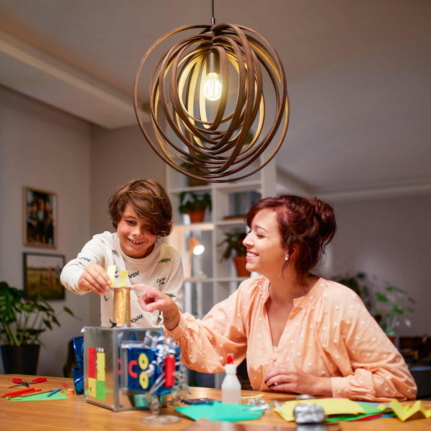 Mère et fils fabriquent un robot en carton et papier pailleté sur une table.