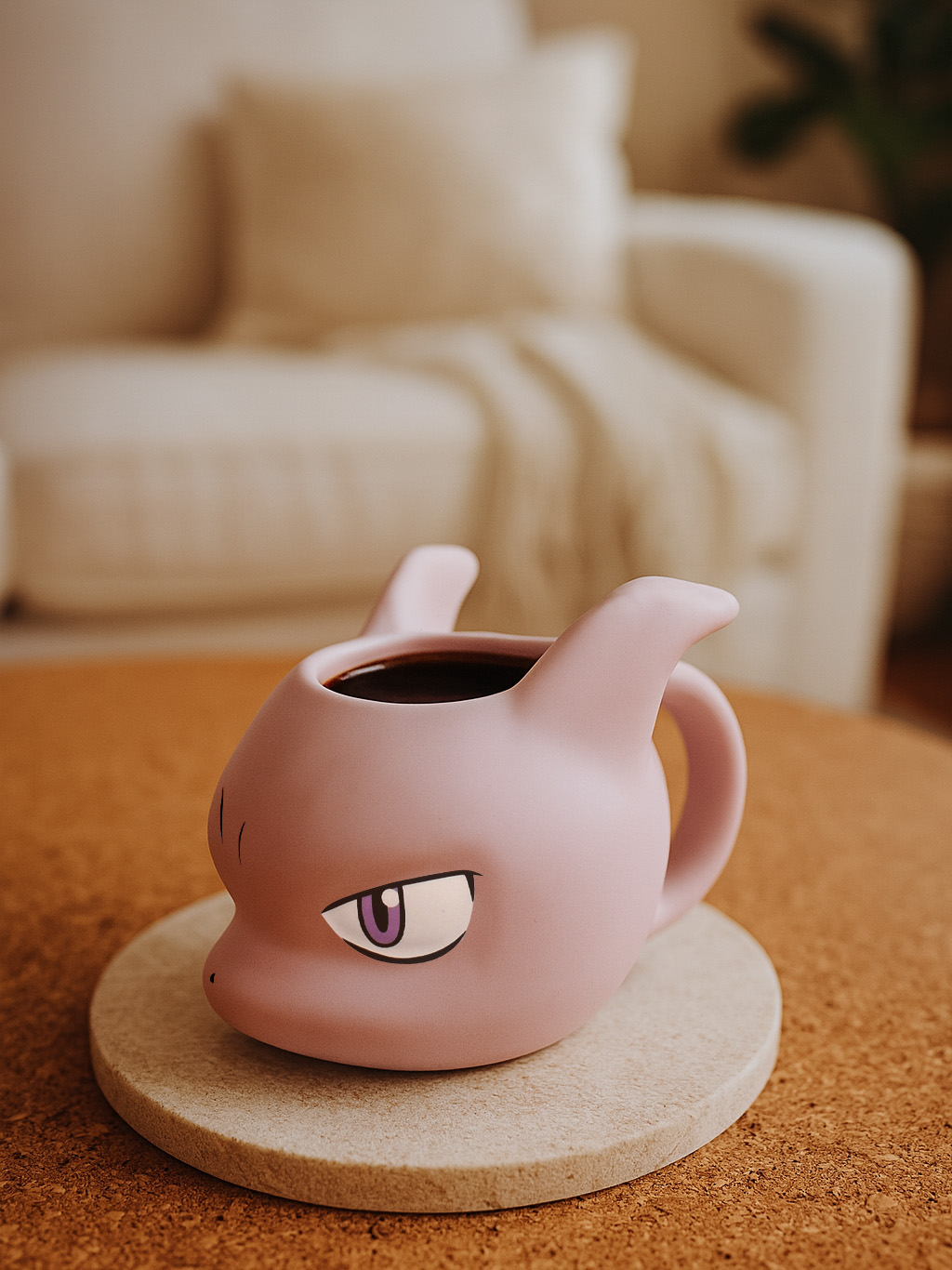 Eine rosa Mewtu-Tasse mit Kaffee steht auf einem Untersetzer.