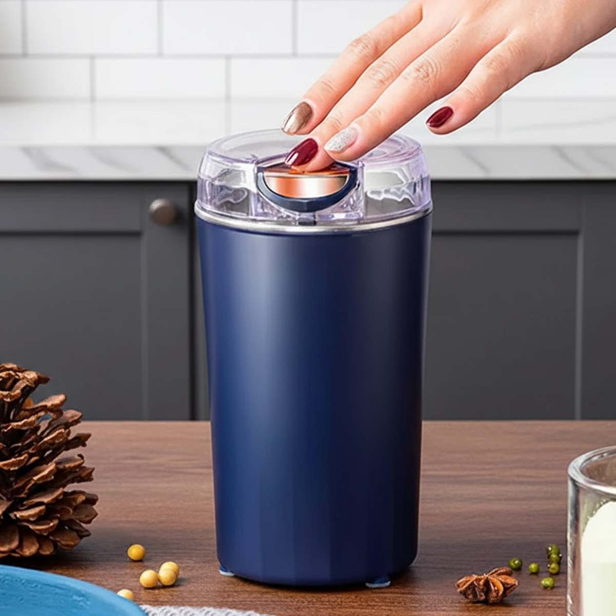 Eine Hand drückt den Knopf eines blauen Kaffeemühlers auf einem Holztisch.