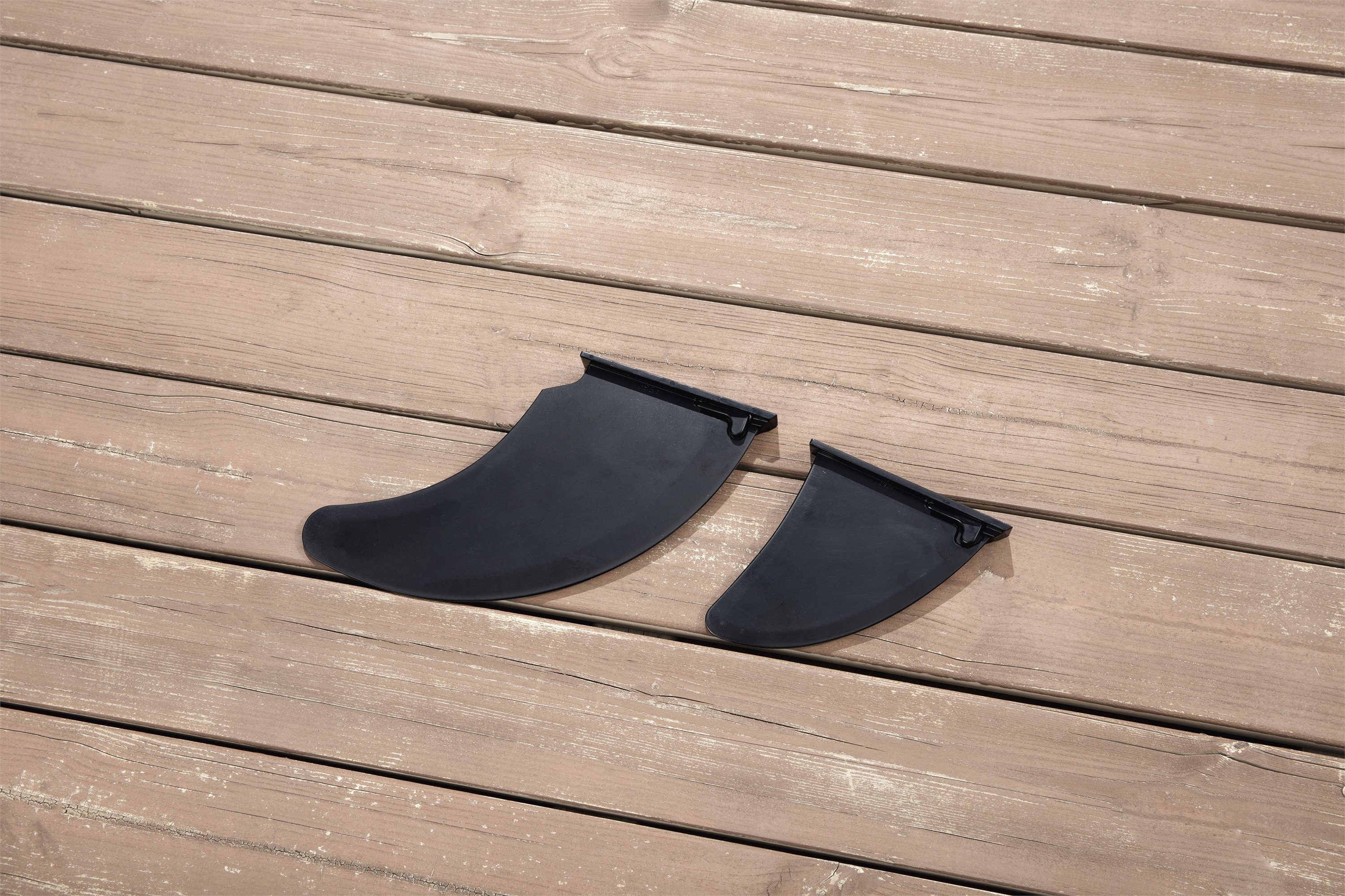 Zwei schwarze Surfbrettflossen liegen auf einem Holzboden.