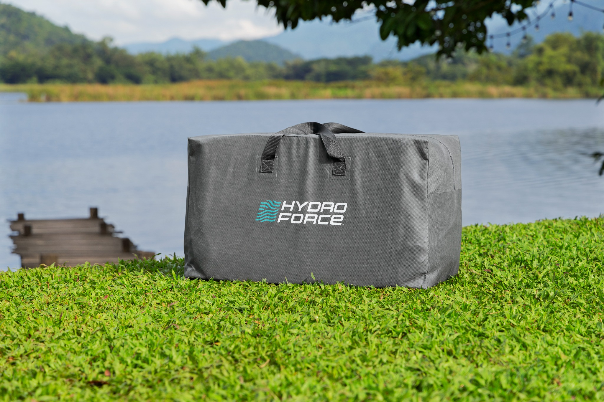 Graue Tasche mit Hydro-Force-Logo auf Gras am Seeufer, Holzsteg im Hintergrund.