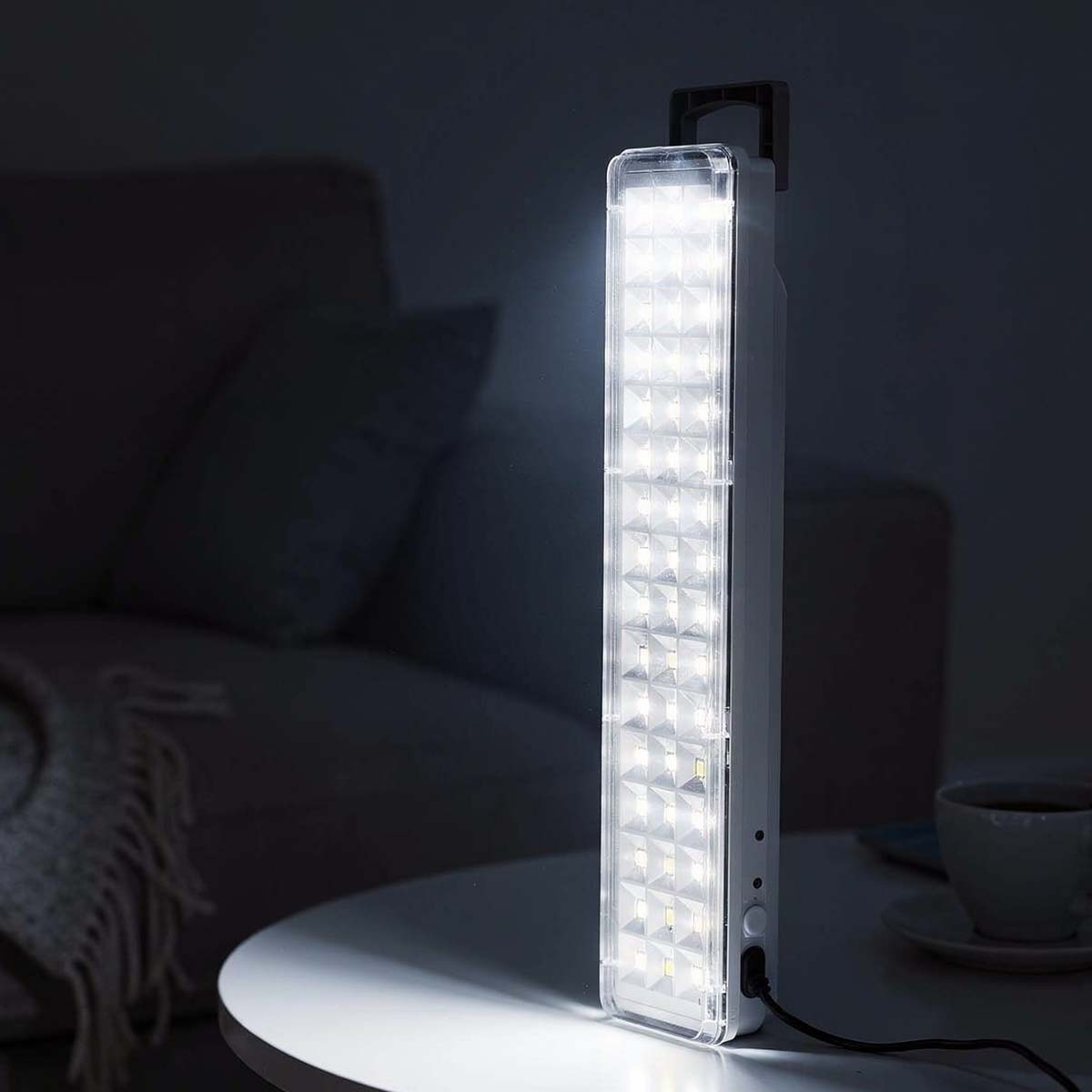 Ein heller LED-Notfallstab auf einem Tisch, daneben eine Tasse Kaffee.