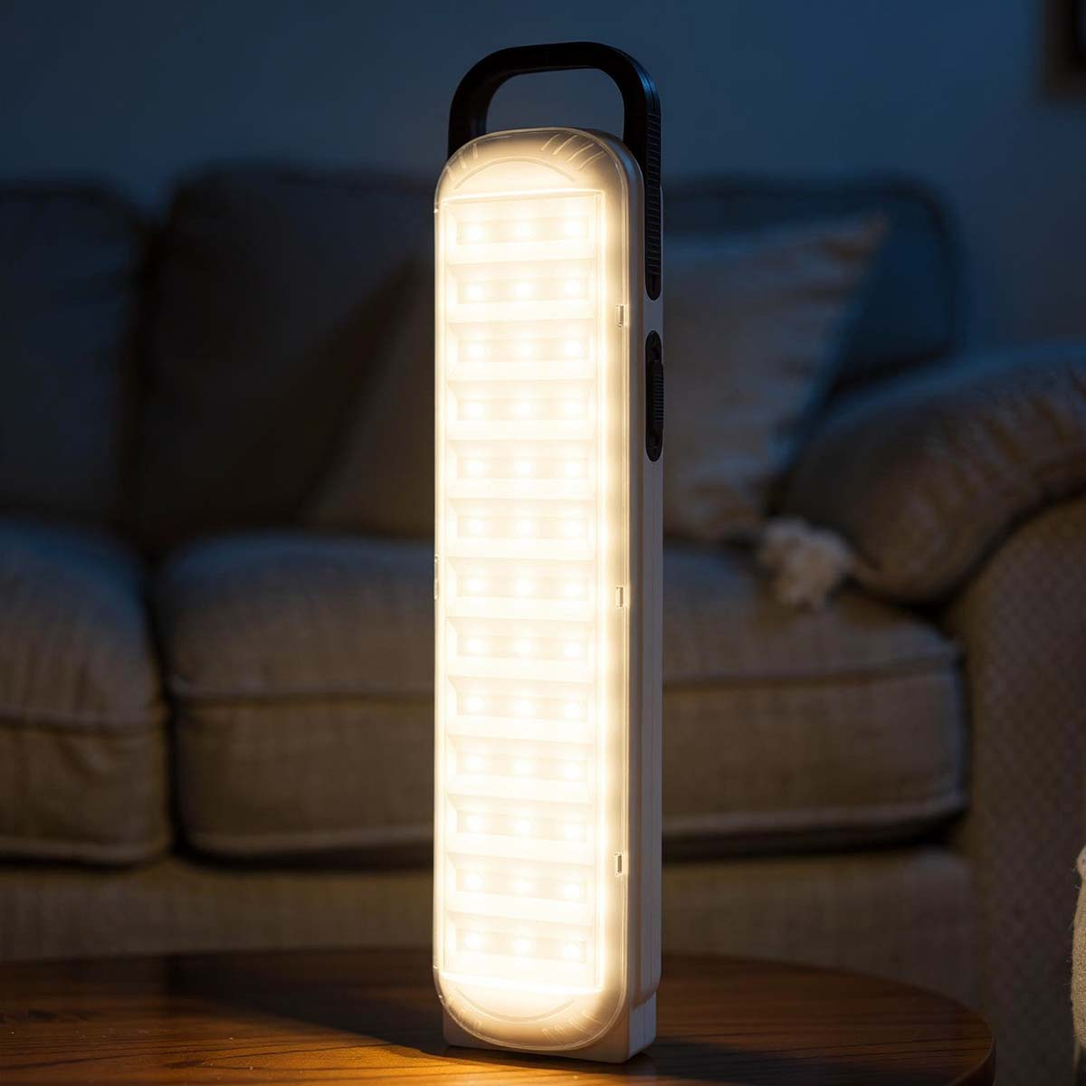 Eine helle, rechteckige Lampe mit Griff steht auf einem Tisch vor einem Sofa.