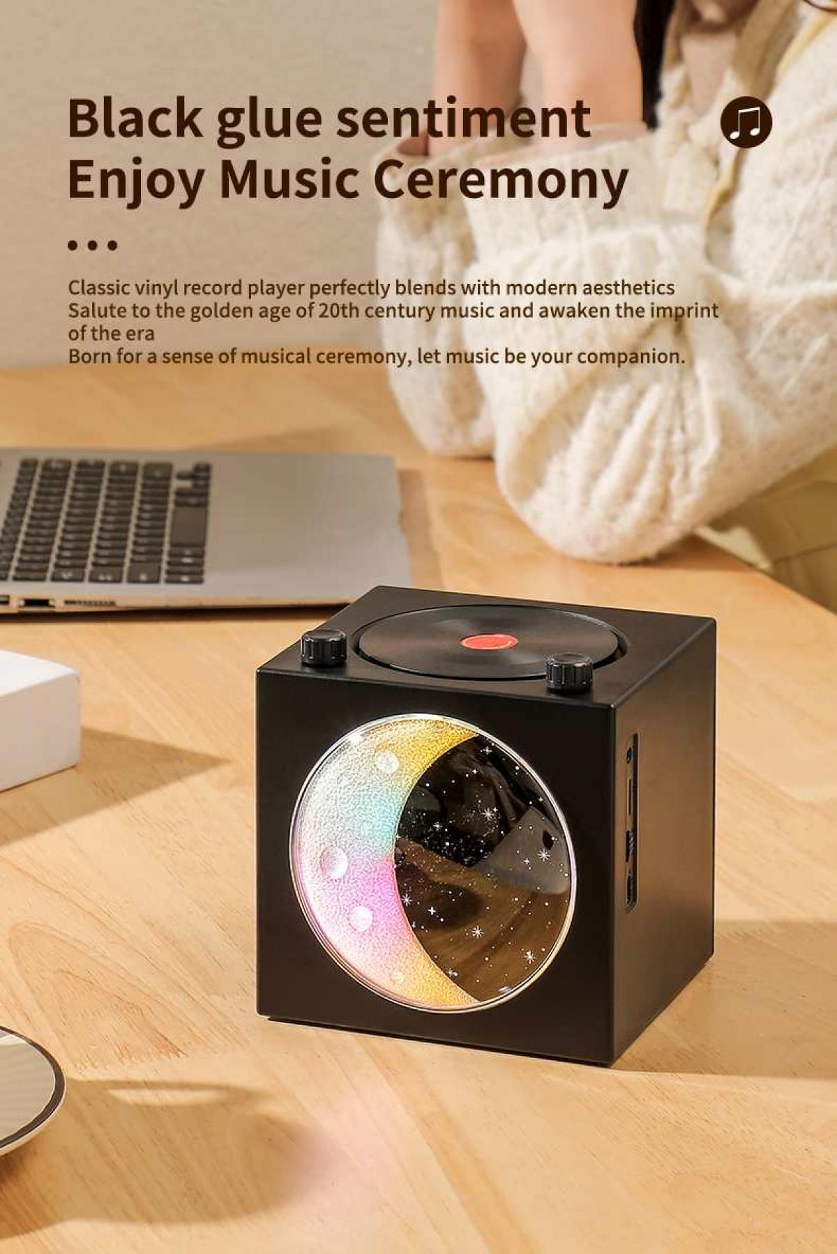 Ein schwarzer Plattenspieler mit Mondlicht-Design steht auf einem Holztisch, neben einem Laptop.