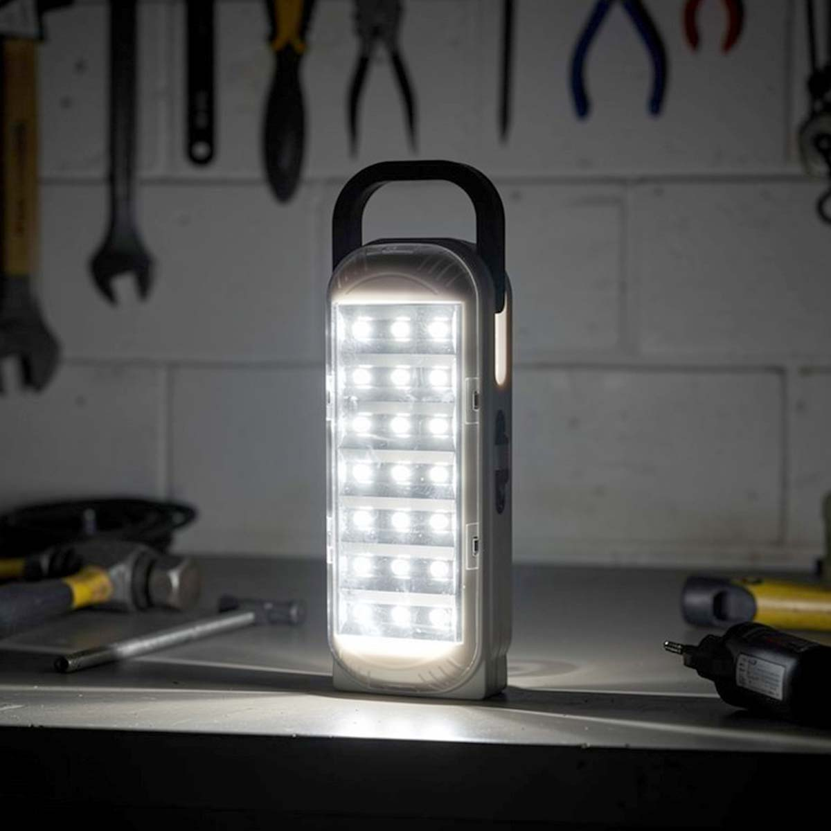 Eine weiße LED-Laterne steht auf einer Werkbank mit Werkzeugen im Hintergrund.