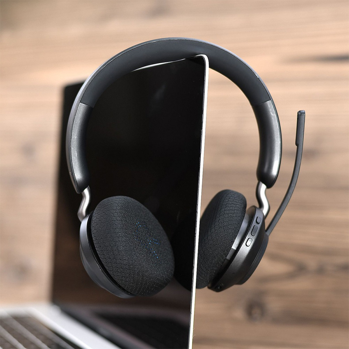 Cuffie nere con microfono poggiate sullo schermo di un laptop. Sfondo in legno.