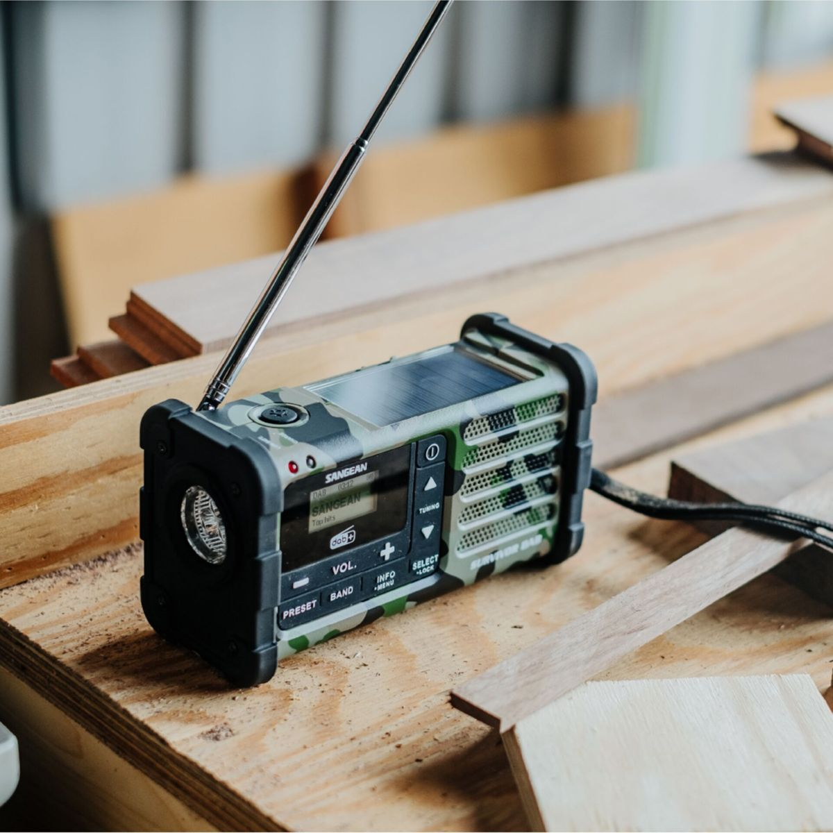 Una radio mimetica con pannello solare, antenna e display su un tavolo di legno.