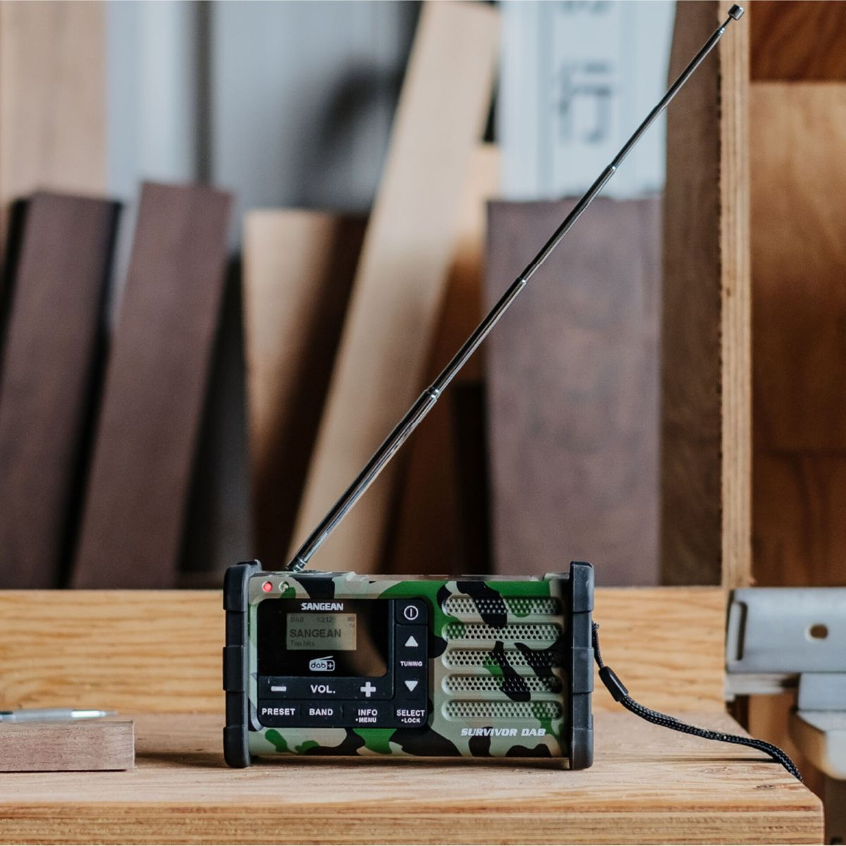 Una radio Sangean Survivor DAB mimetica con antenna estesa è su un tavolo di legno.