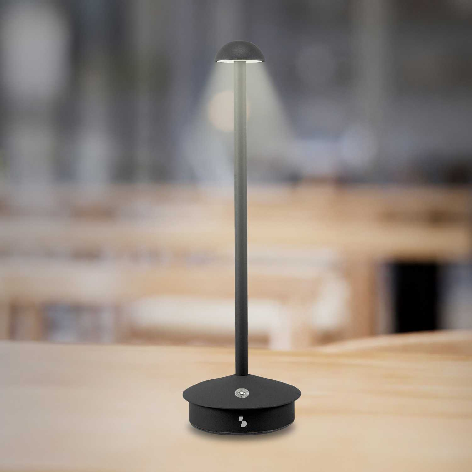 Una lampada da tavolo nera con base rotonda e paralume regolabile su tavolo di legno.