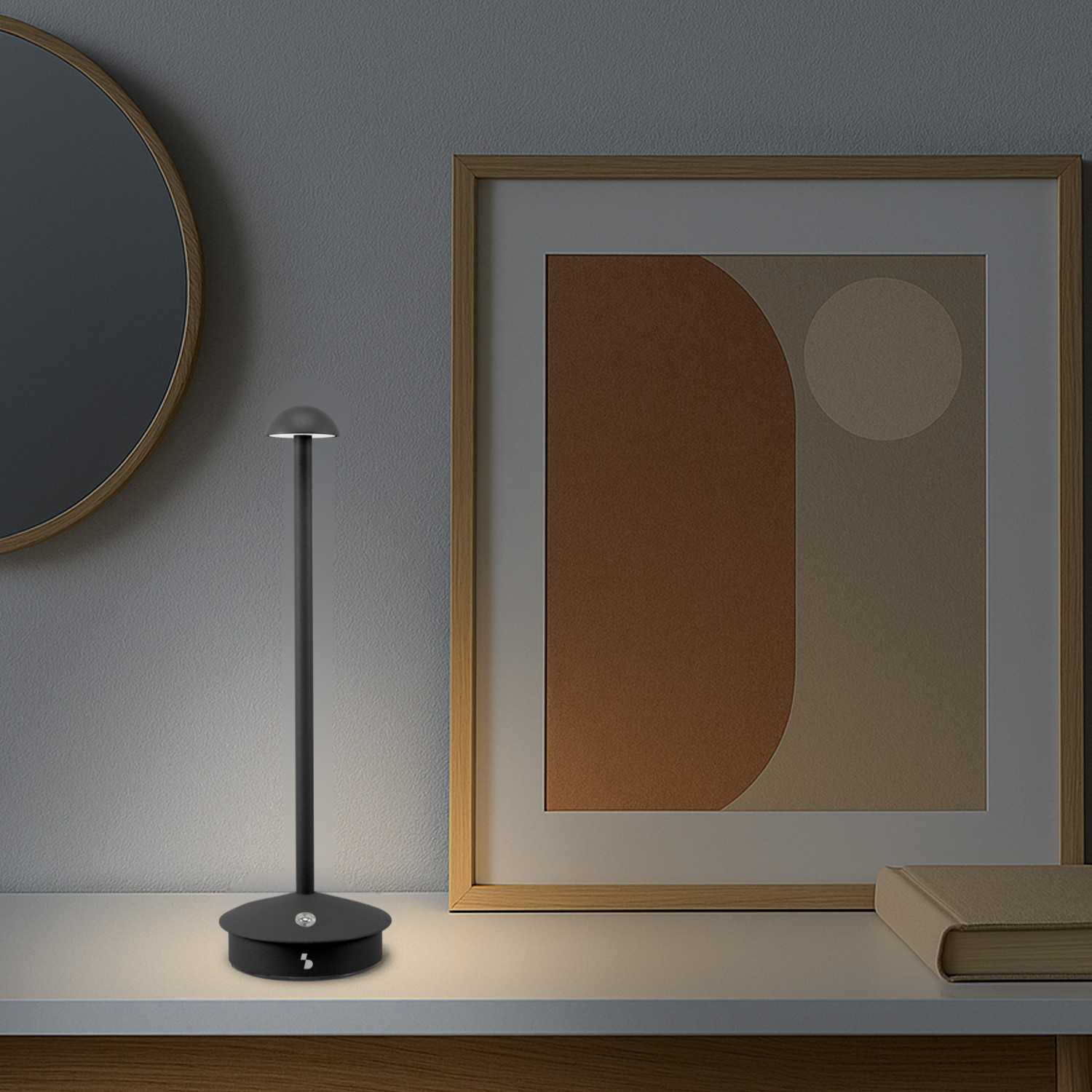 Una lampada nera ed elegante si trova su un tavolo accanto a uno specchio e un quadro.