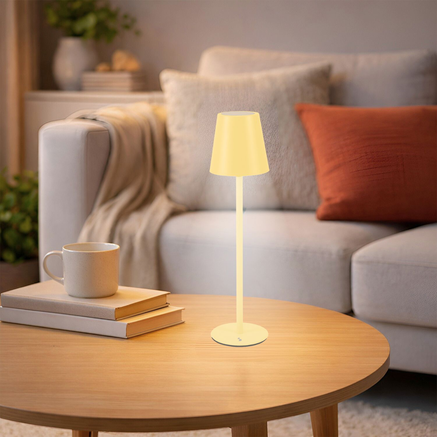 Lampada gialla su tavolo in legno con libri e tazza. Divano sullo sfondo.
