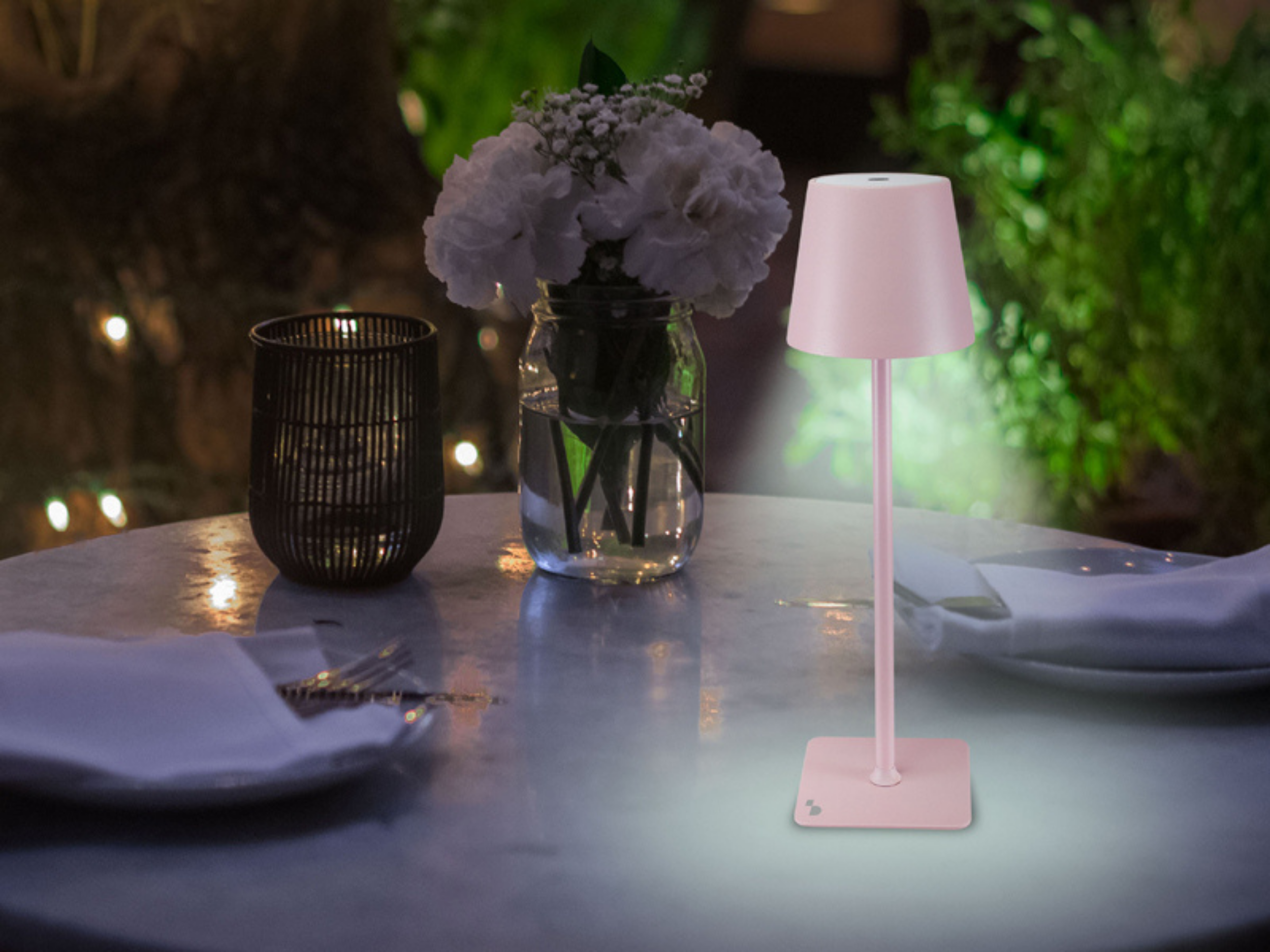 Una lampada da tavolo rosa è su un tavolo con fiori e un portacandele.