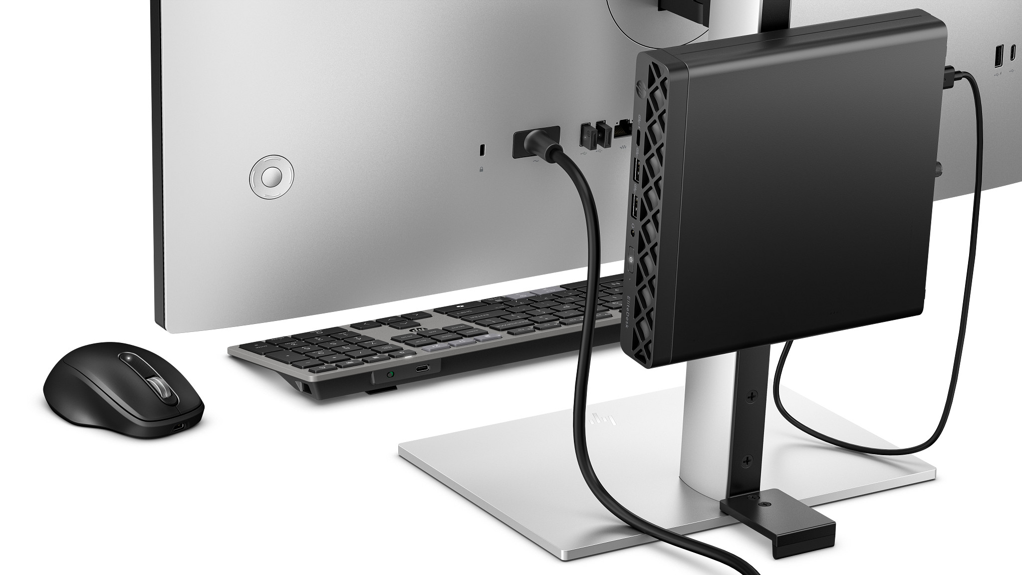 Un mini PC nero è attaccato a un monitor argento. Tastiera e mouse davanti.