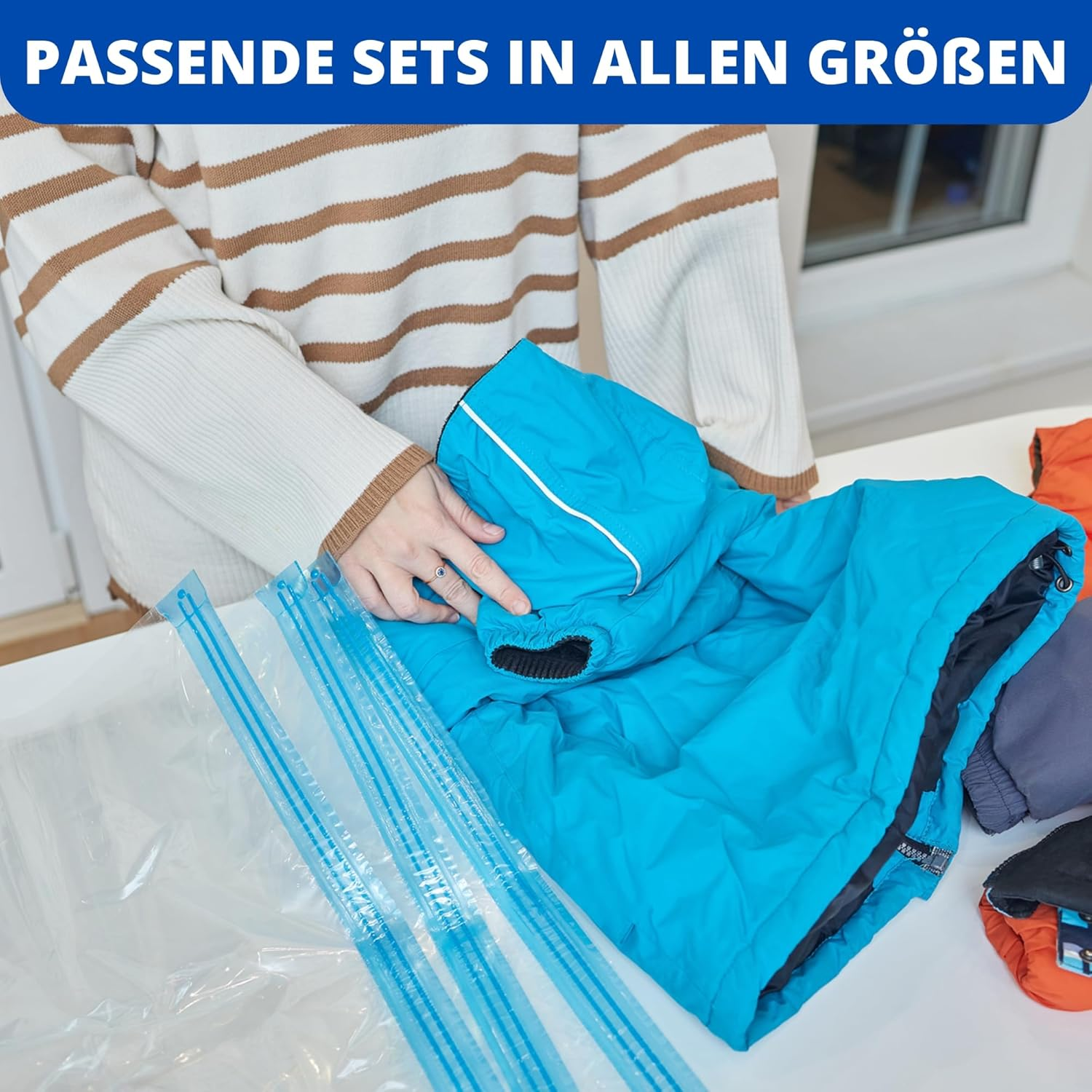 Eine Person packt eine blaue Jacke in einen Vakuumbeutel. Mehr Kleidung liegt daneben.