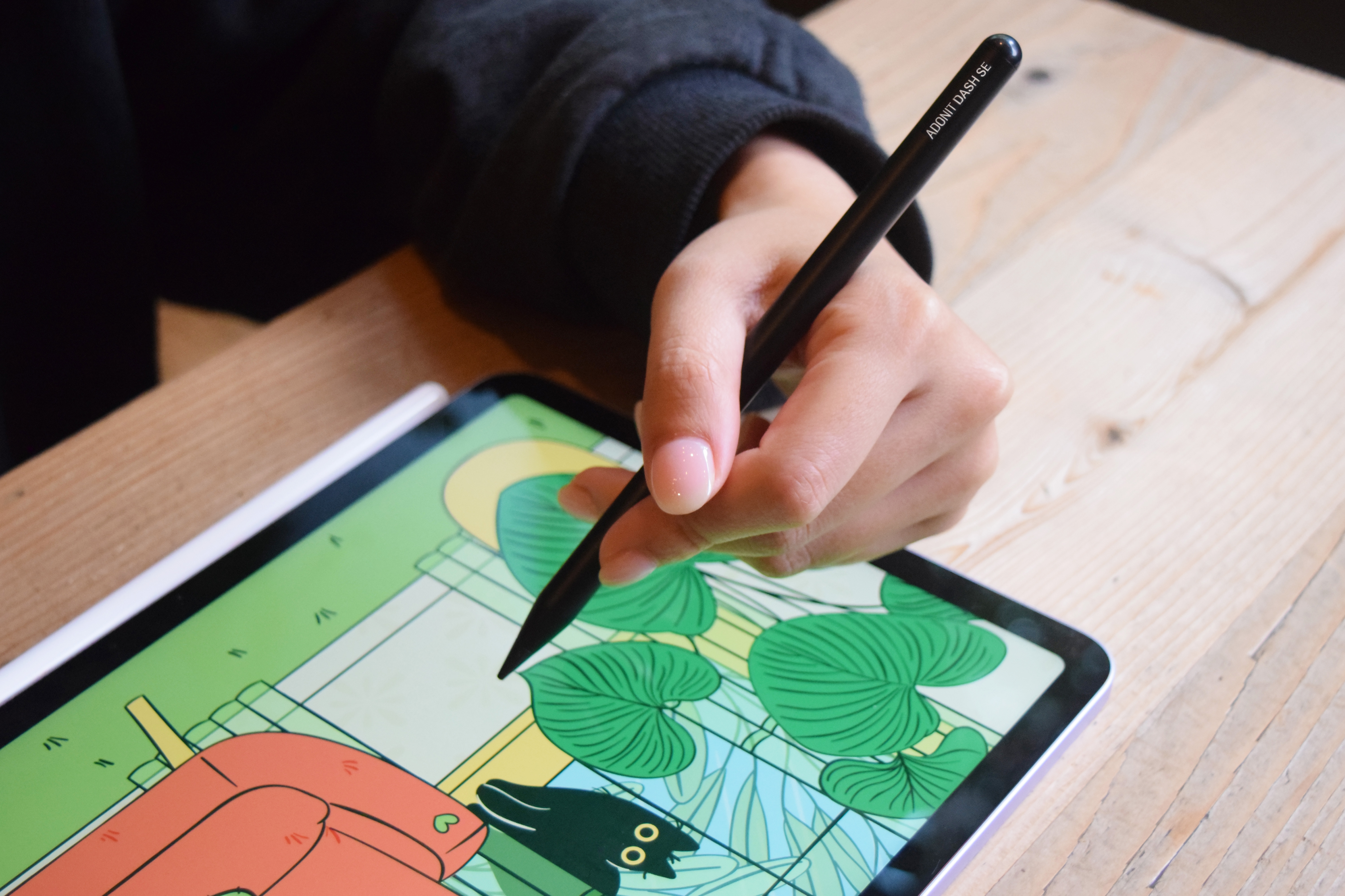 Una mano tiene uno stilo nero su un tablet che mostra un disegno colorato.