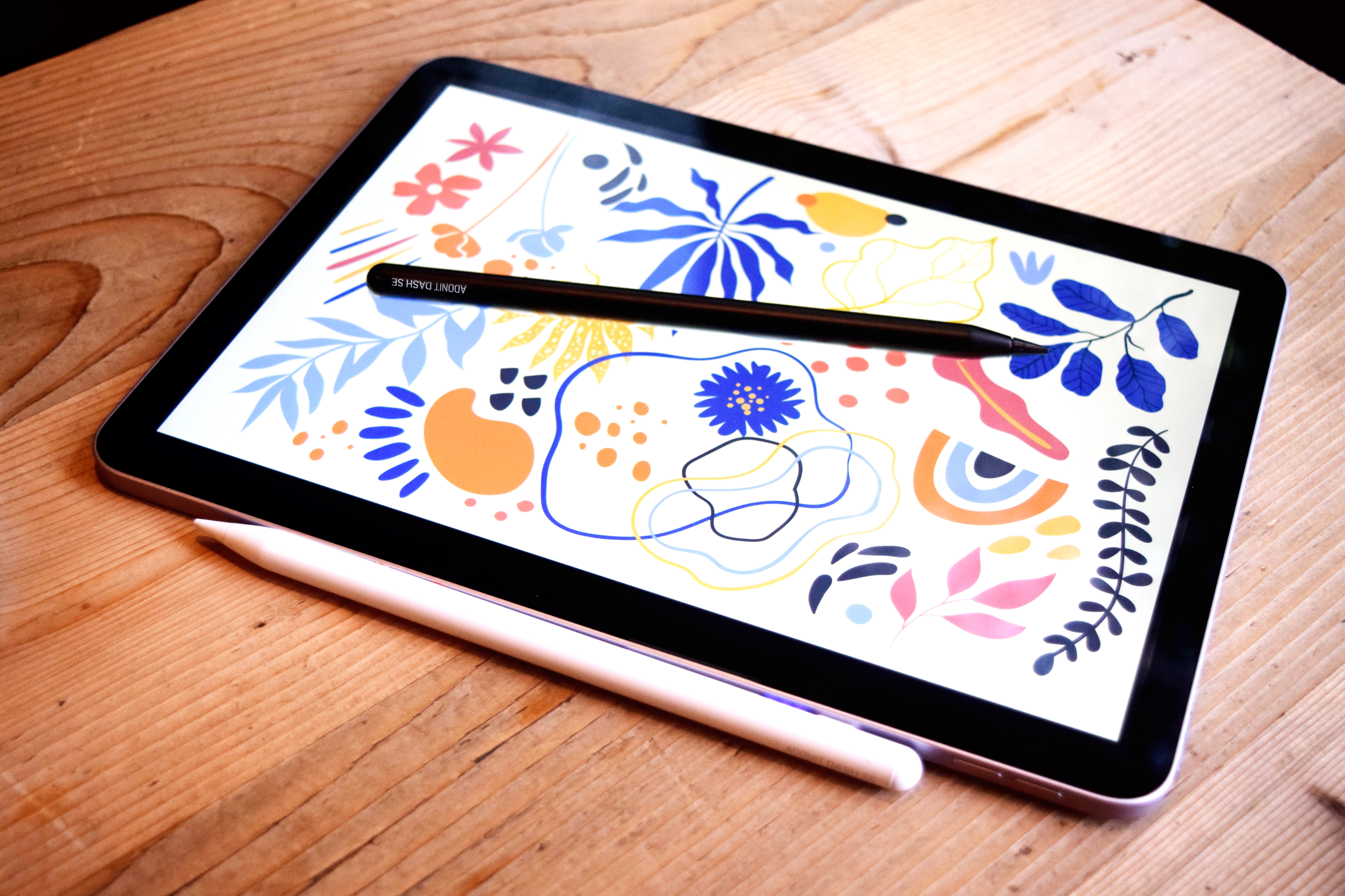 Un tablet con motivo colorato e due pennini su un tavolo di legno.