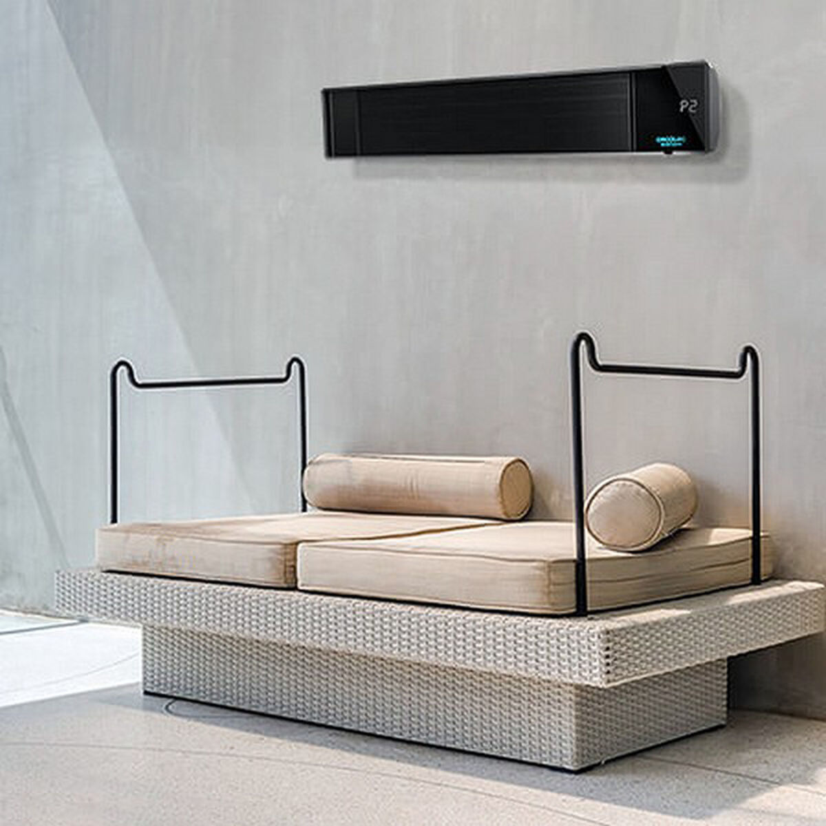 Czarny grzejnik nad beżową sofą z poduszkami na szarym tle.