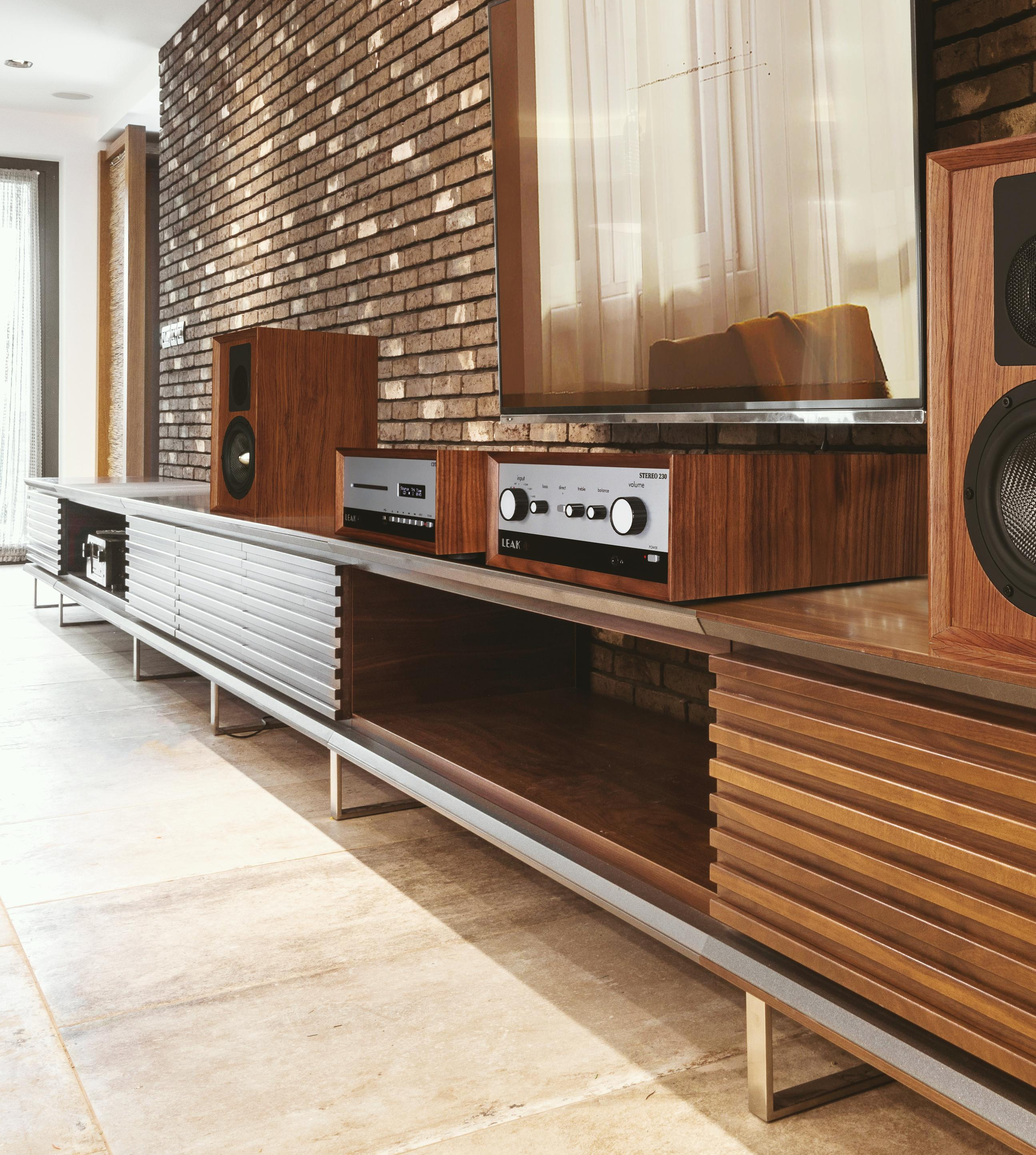 Houten luidsprekers en stereo-installatie op een mediameubel voor een bakstenen muur.