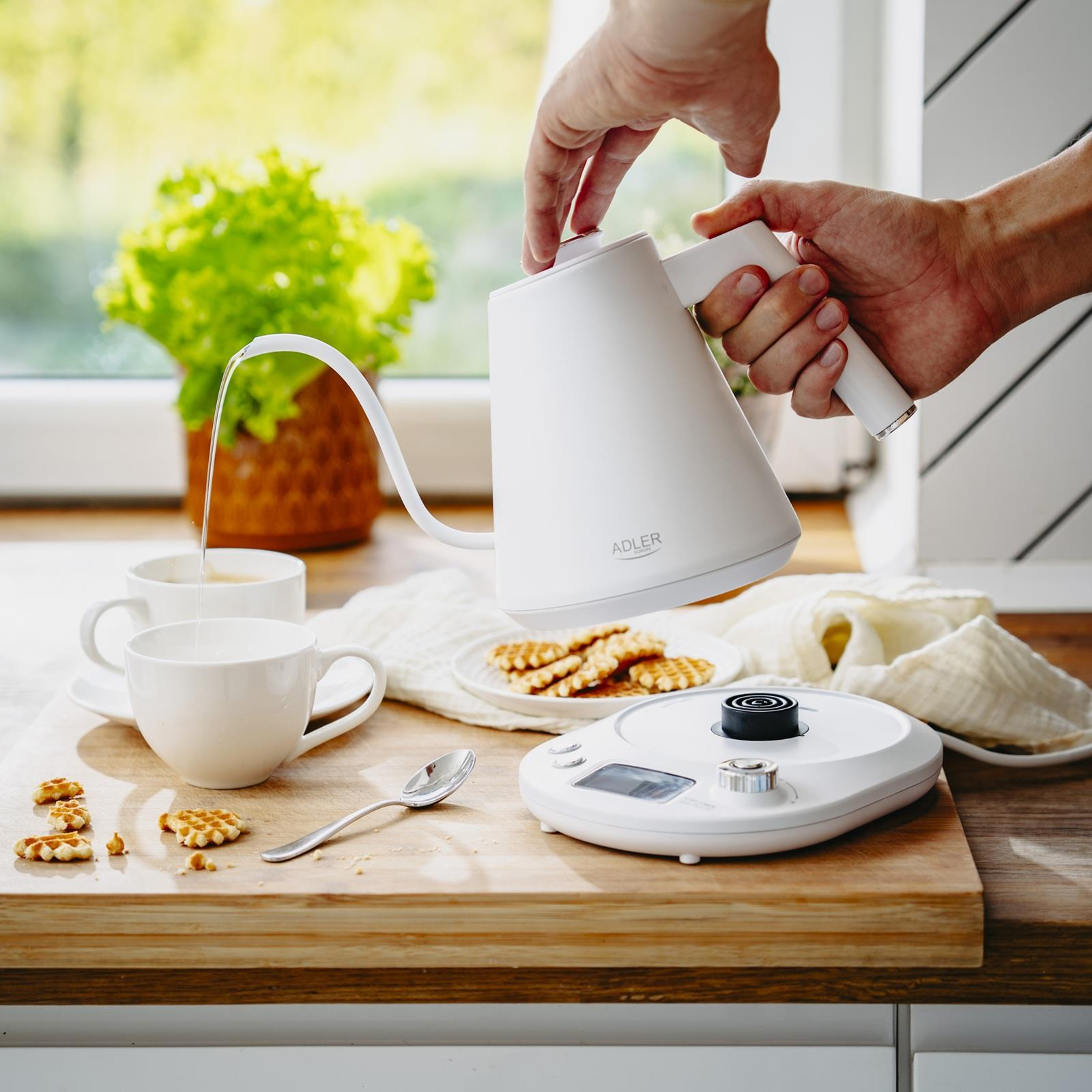 Hände gießen Wasser aus einem weißen Kessel in eine weiße Tasse.