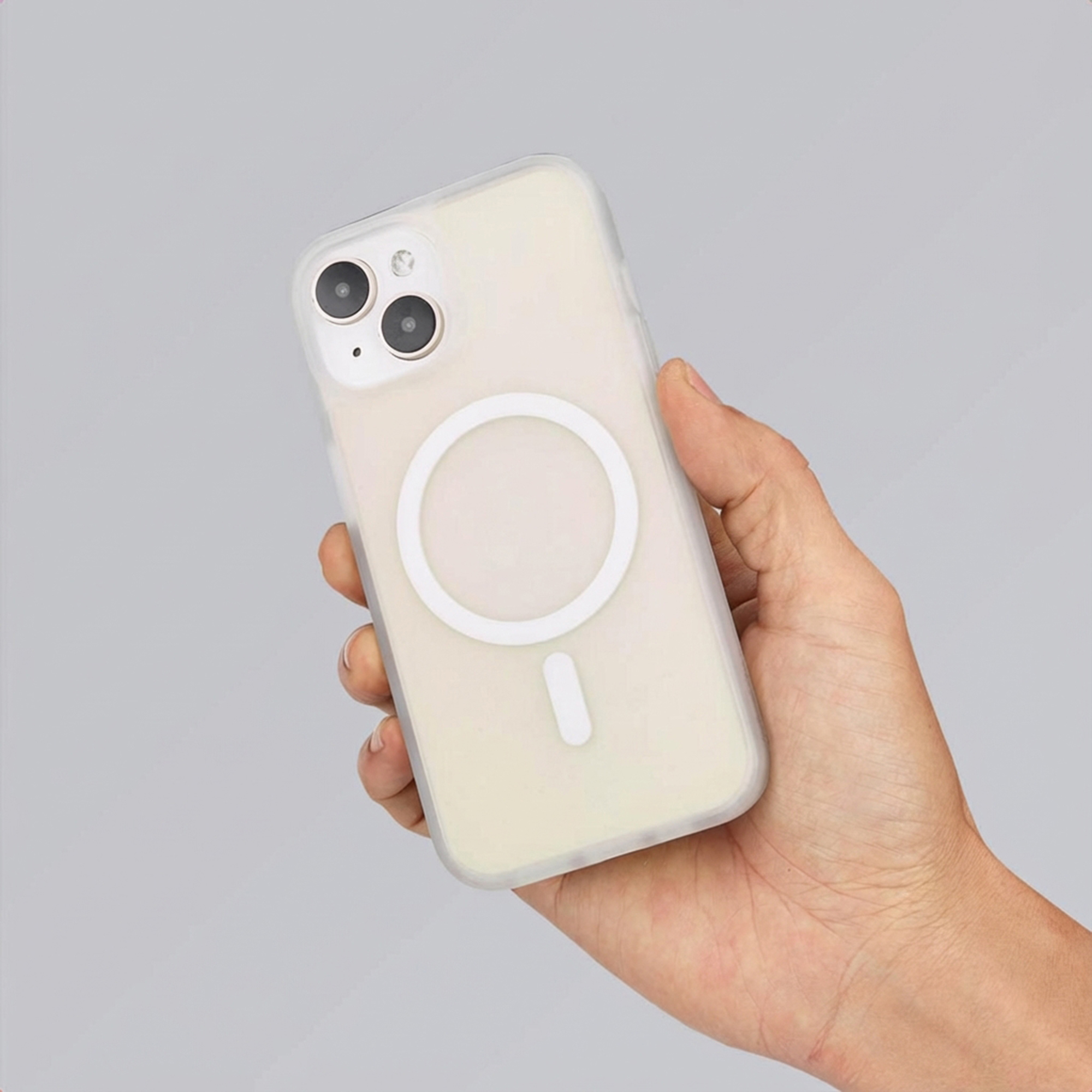 A hand holds a translucent phone case with a white MagSafe ring on a gray background.