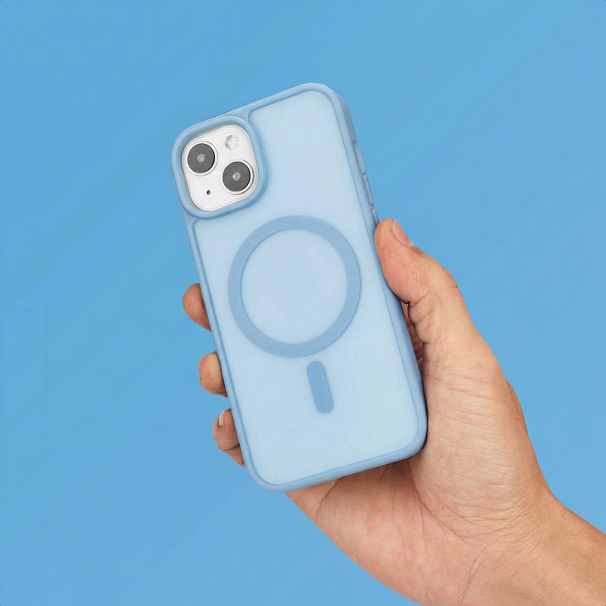 Een hand houdt een lichtblauwe telefoonhoes met MagSafe-cirkel vast tegen blauwe achtergrond.