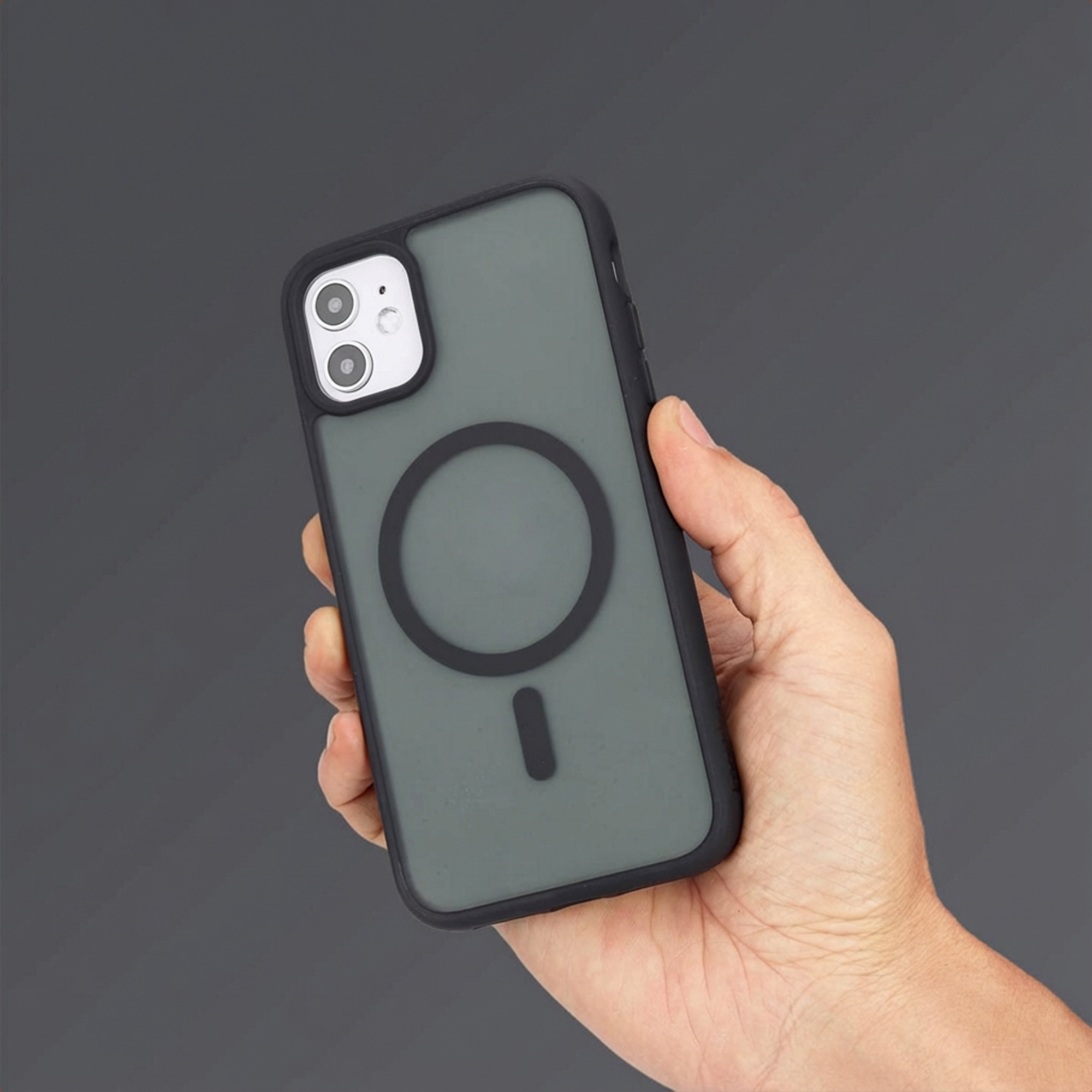 Main tenant une coque de téléphone gris foncé avec bordure noire et cercle de charge magnétique.