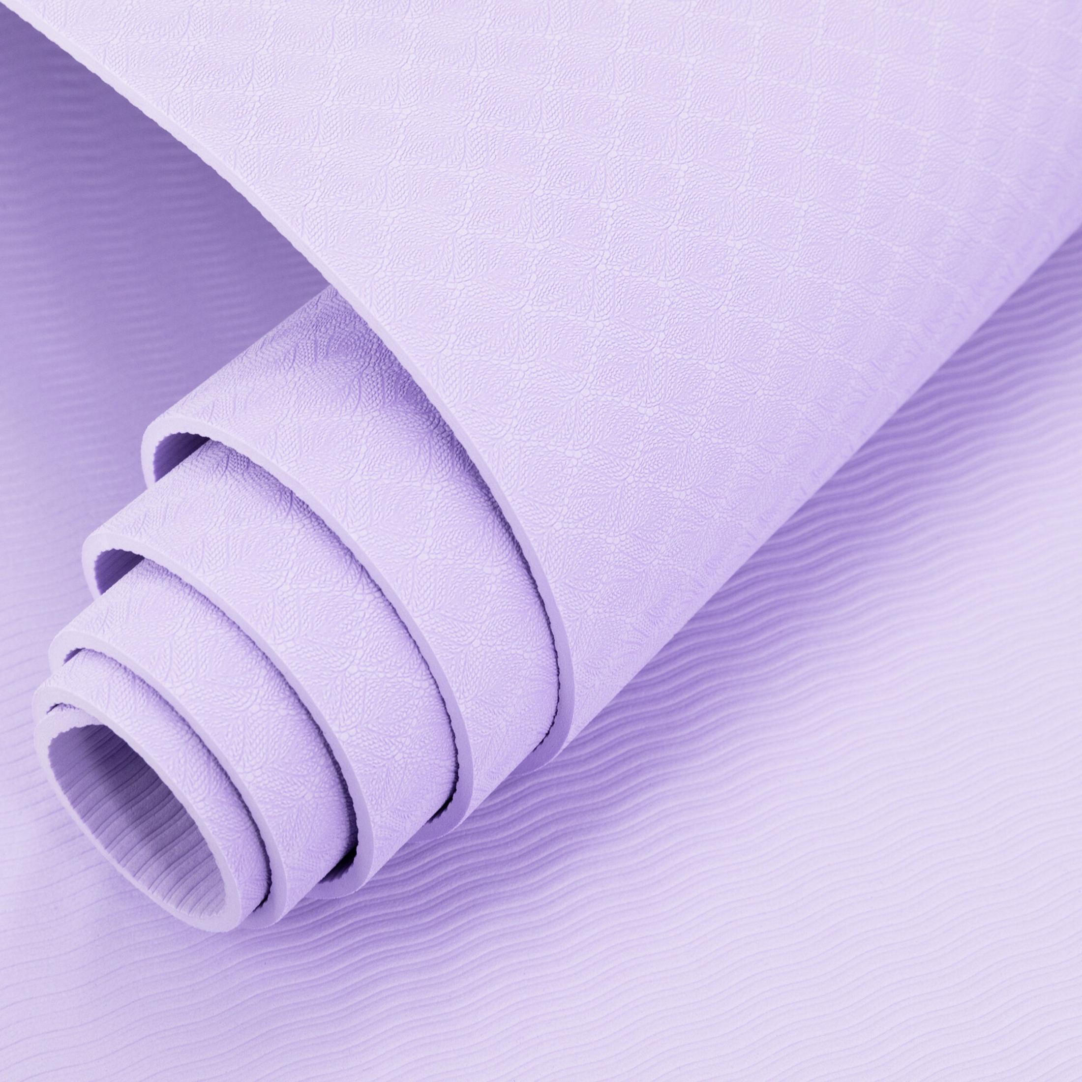 Una esterilla de yoga morada enrollada con un patrón de hojas sobre una superficie morada ondulada.