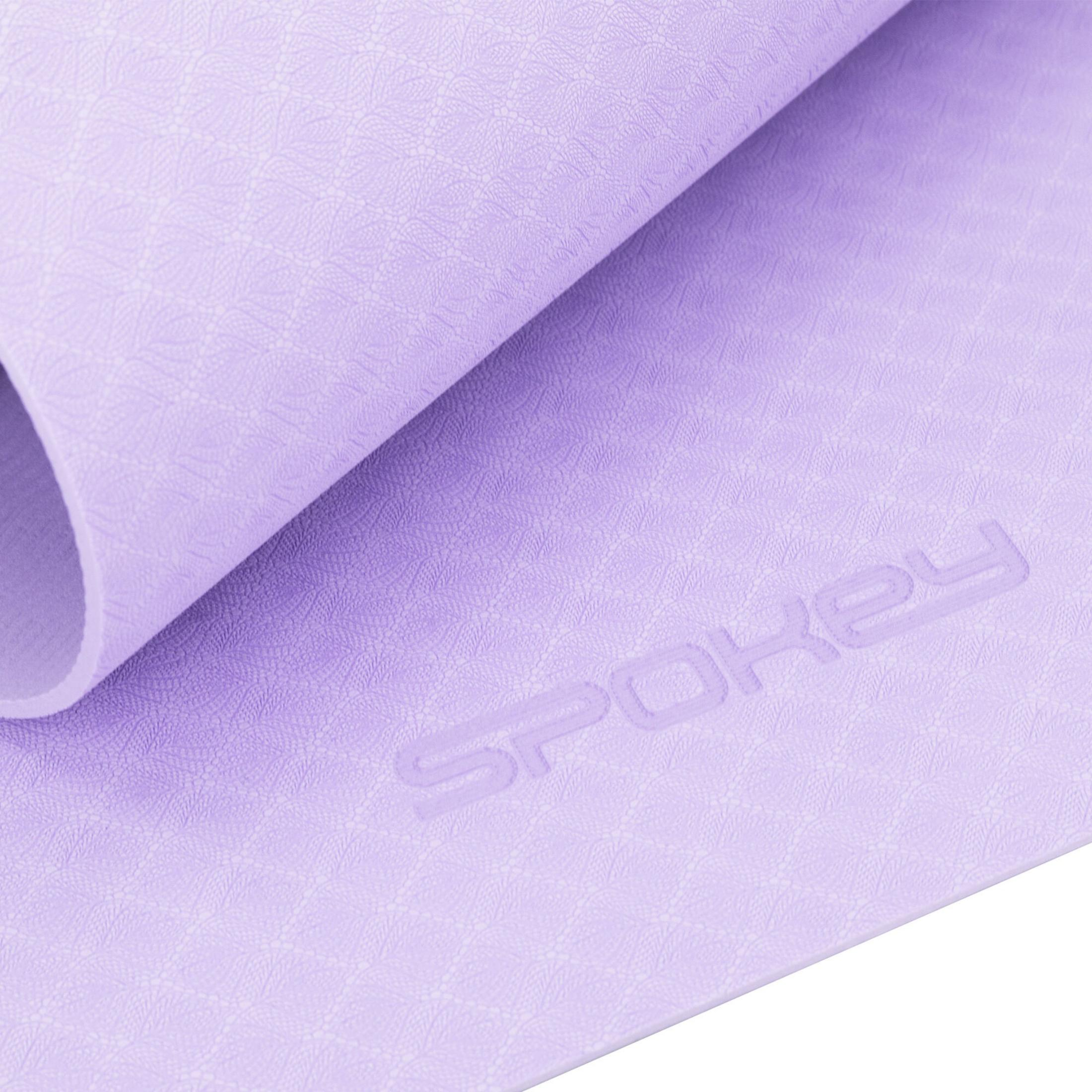 Una esterilla de yoga lila con logo Spokey y estampado de hojas.