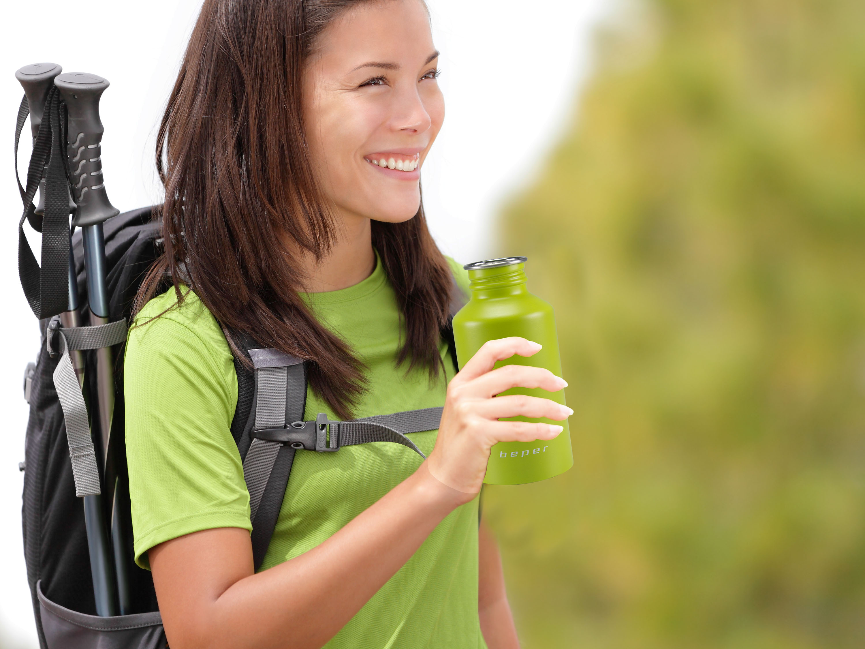 Una donna con zaino e bastoncini da trekking beve da una bottiglia verde.