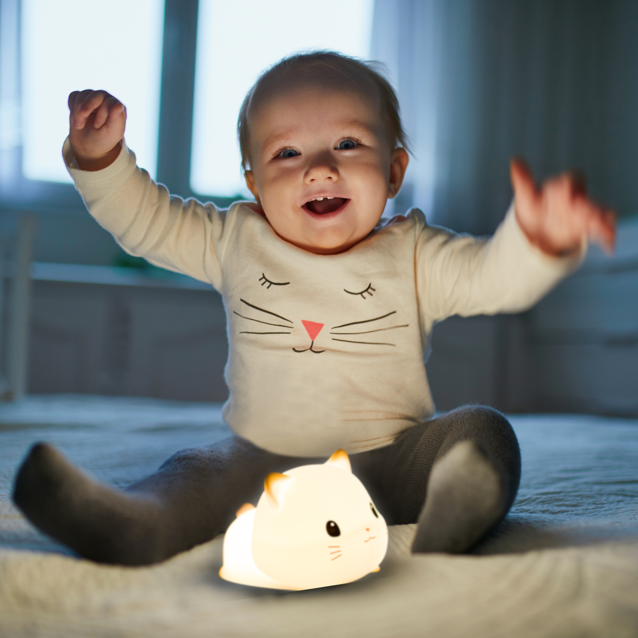 Ein Baby sitzt auf einem Bett mit einem niedlichen Nachtlicht in Form eines Hamsters.